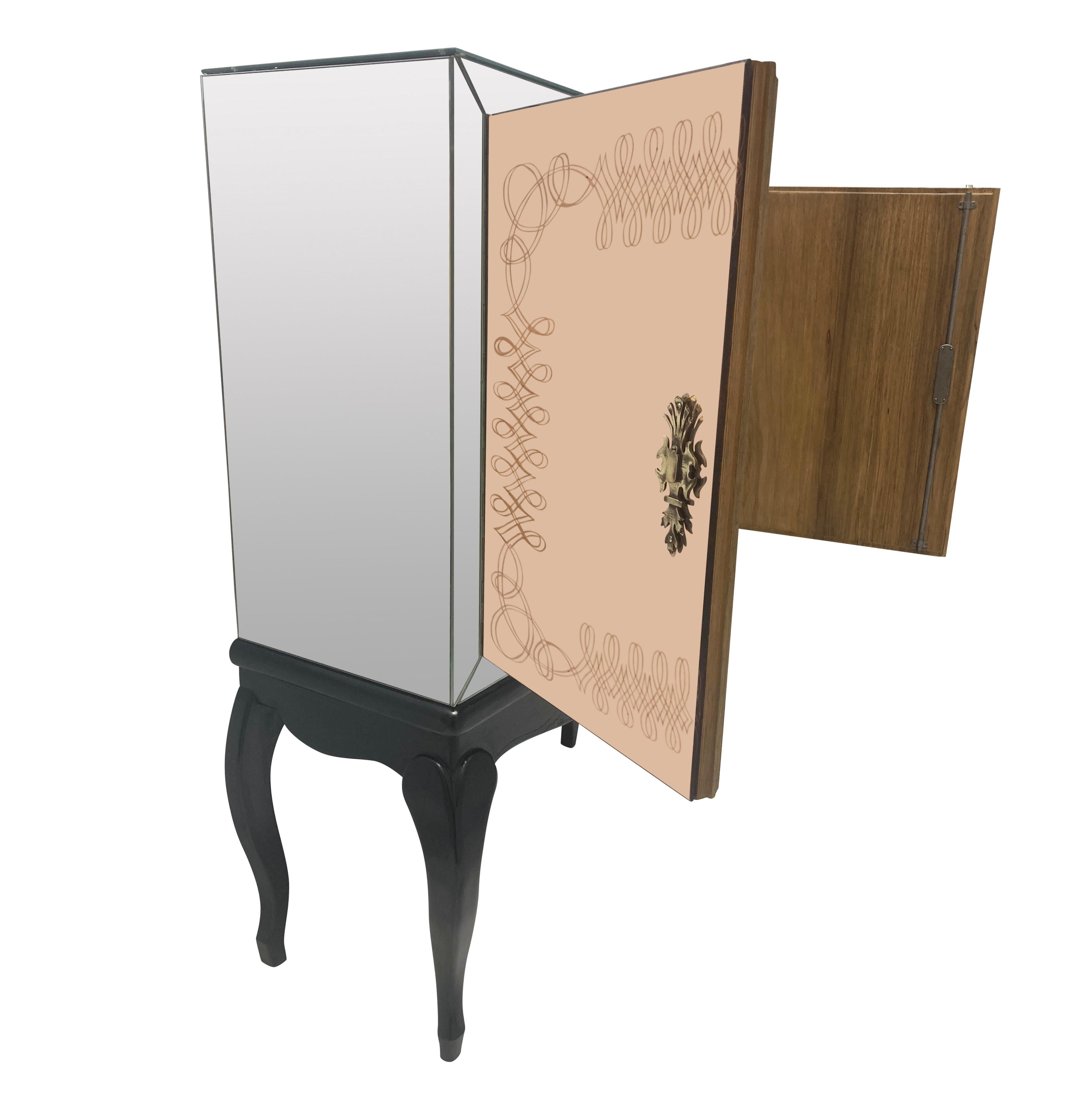 Fino mueble bar francés de mediados de siglo sobre peana. El armario con espejo de paneles lisos sujetos con rosetas de cristal, con las dos puertas de espejo rosa con diseño de roleos. Las asas y escudetes en bronce y todo el interior en madera de