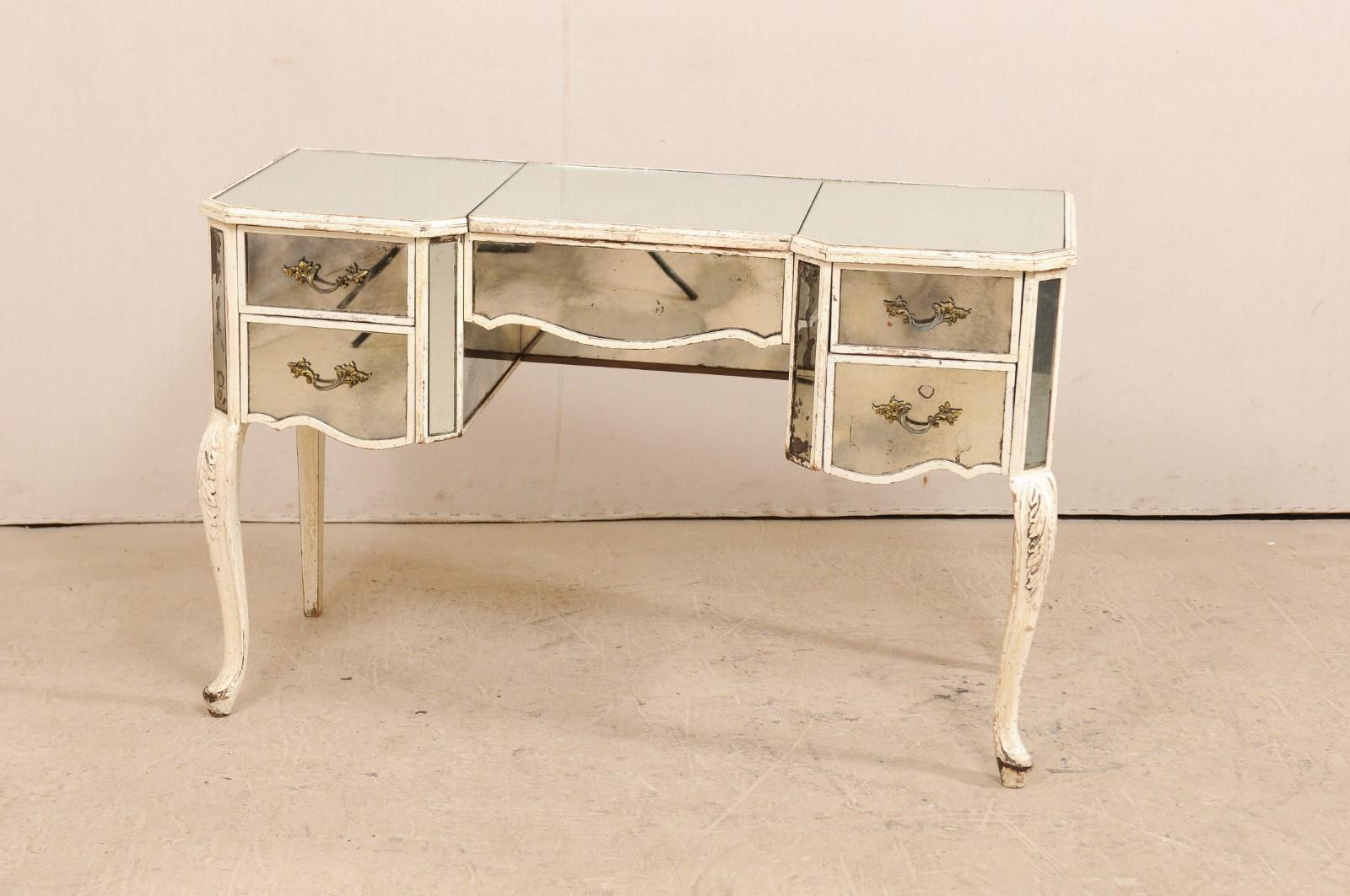 A French mid-century mirrored dressing table. This beautiful French vanity is adorned in a mirrored exterior, with sweetly designed lines, canted side posts, accented with old white paint, and presented upon slender cabriole legs with acanthus