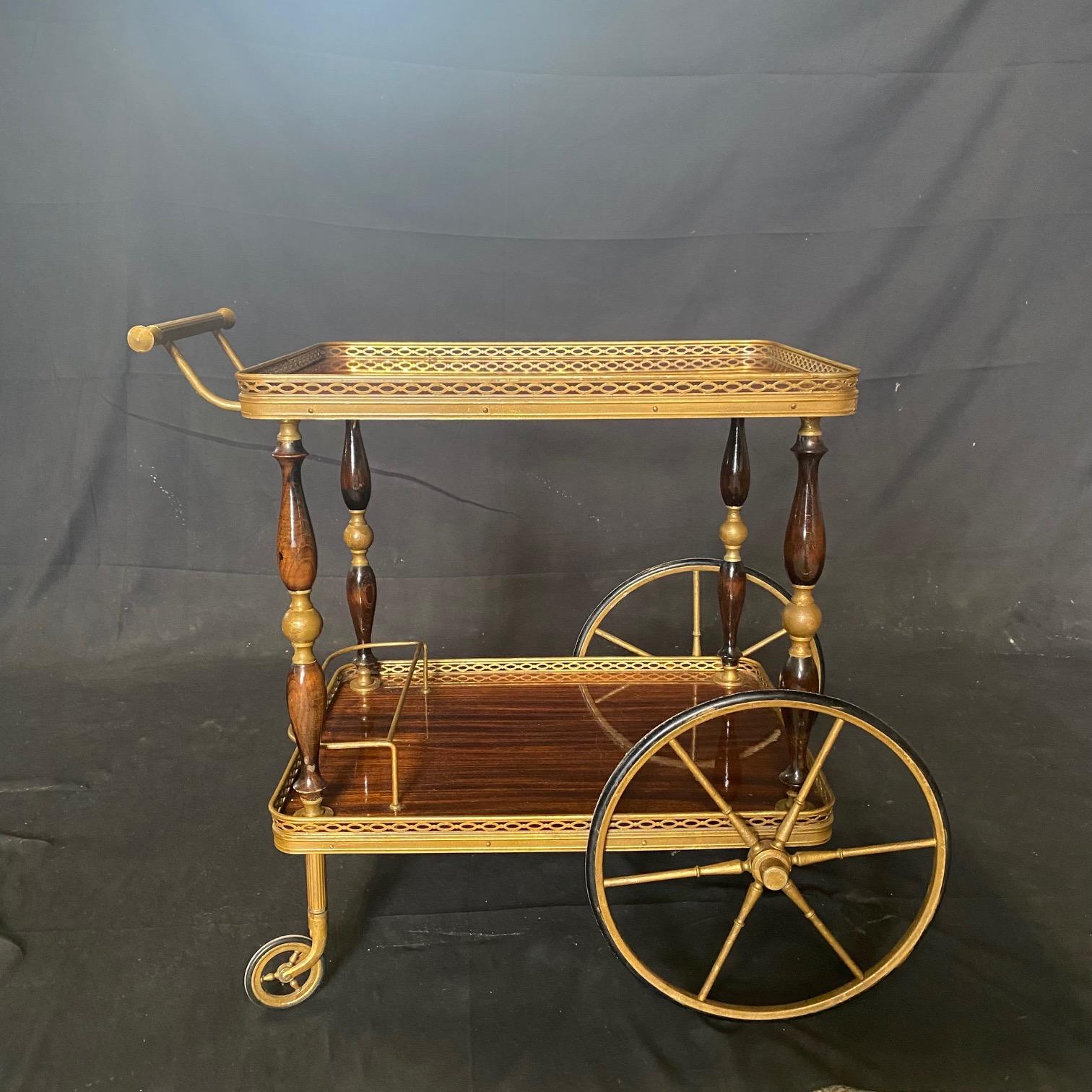 Luxurious French brass bar trolley cart in beautiful neoclassical style from the 1950s. Two formica serving tiers that look like rosewood with a delicate brass decorative edge all around the sides of each tier. The lower tier tray has a brass bottle