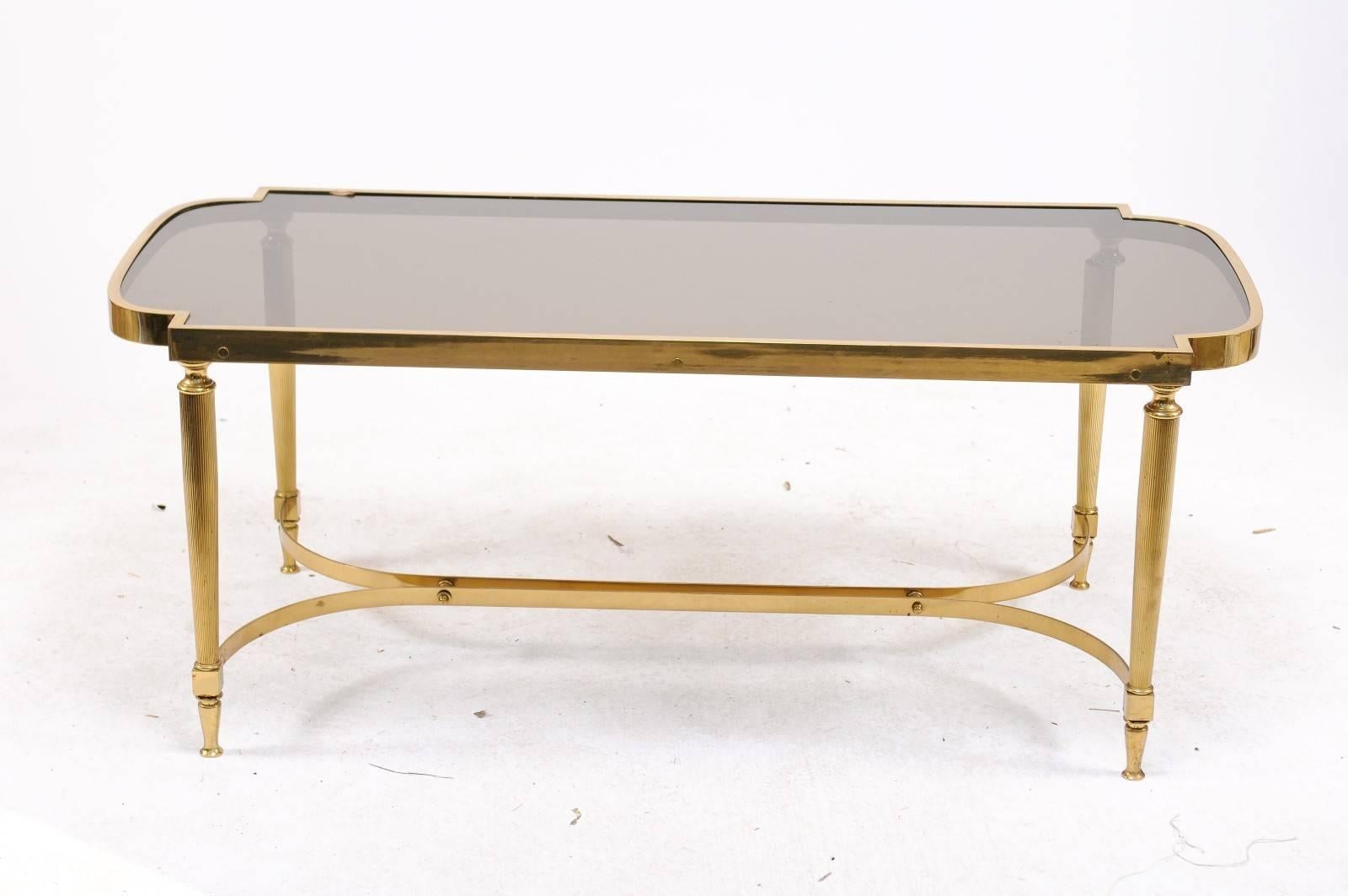 A vintage French bronze coffee table with smoked glass top, reeded legs and double curved cross stretcher from the second half of the 20th century. It was the shape of this vintage 1970s Parisian coffee table that first got our attention, along with