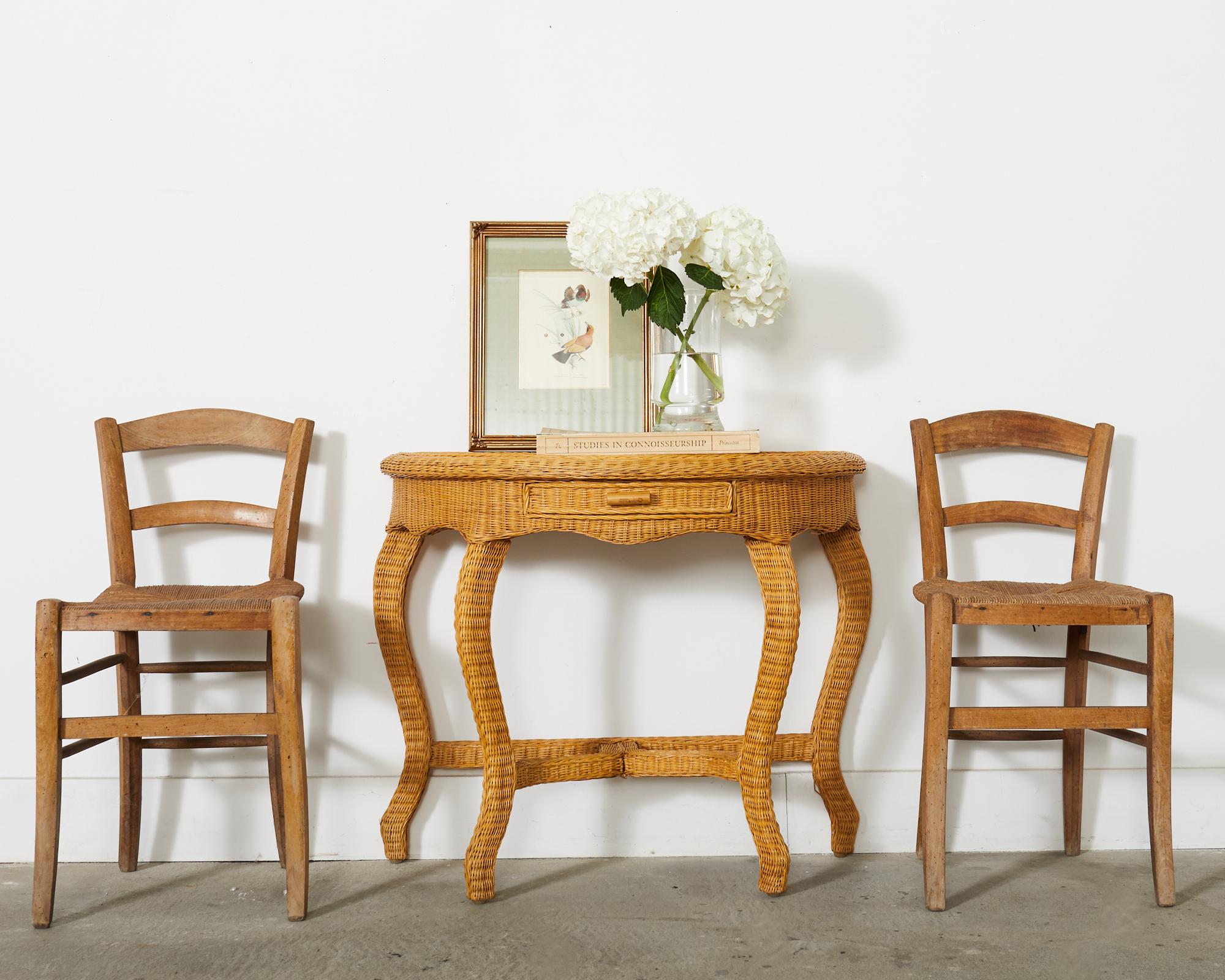 Charming mid-century organic modern demi-lune console table featuring a wood frame covered with fine woven wicker. The table has a small braided gallery edge around the top border. The console is fronted by a small storage drawer in the middle with