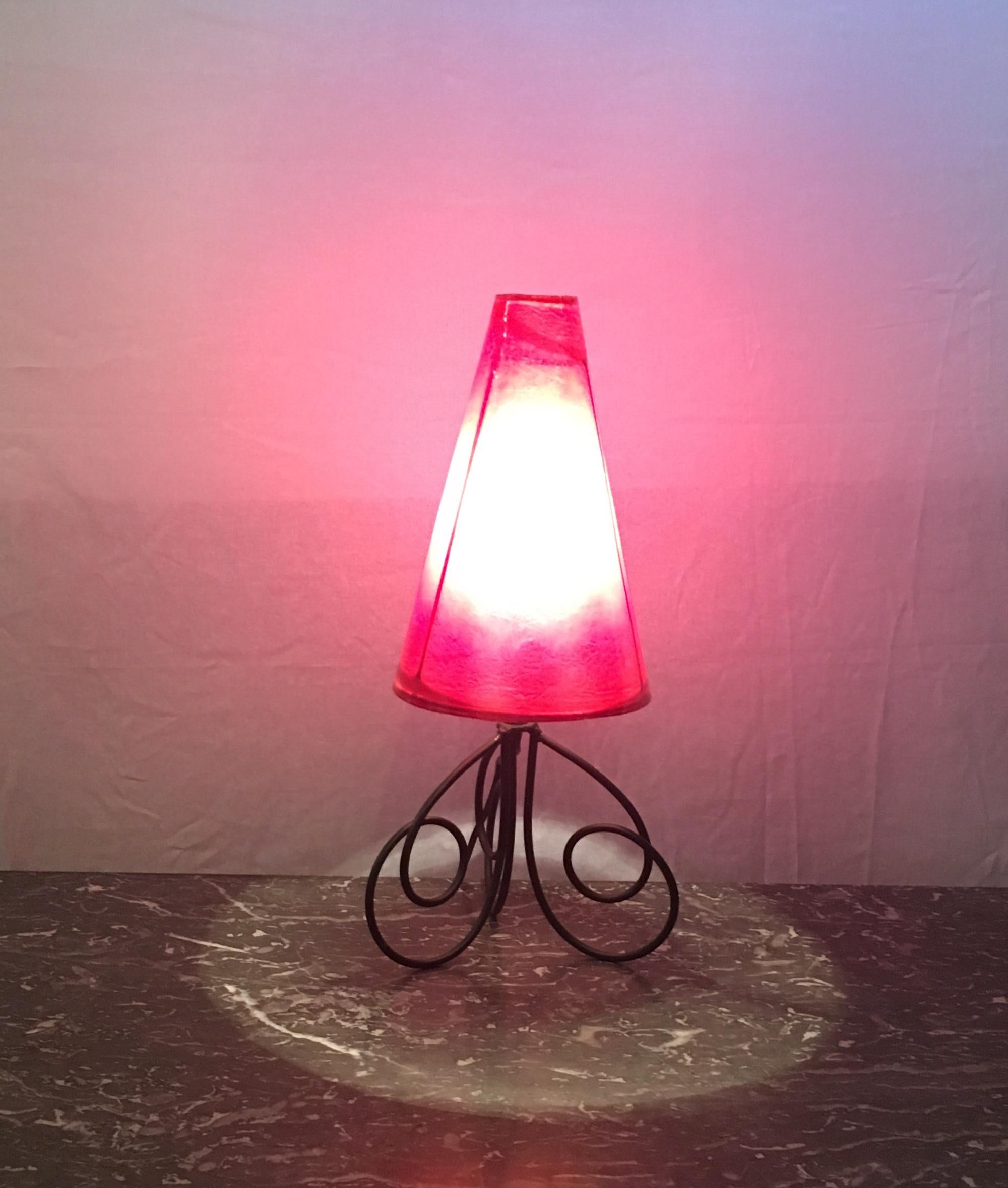 French 1960s table lamp with wrought iron base and orange/red color shade made of a special fiberglass. Shade is removable. 

Nice soft lighting and very stylish.
We photographed the lamp when lit using two different white bulbs therefore achieving