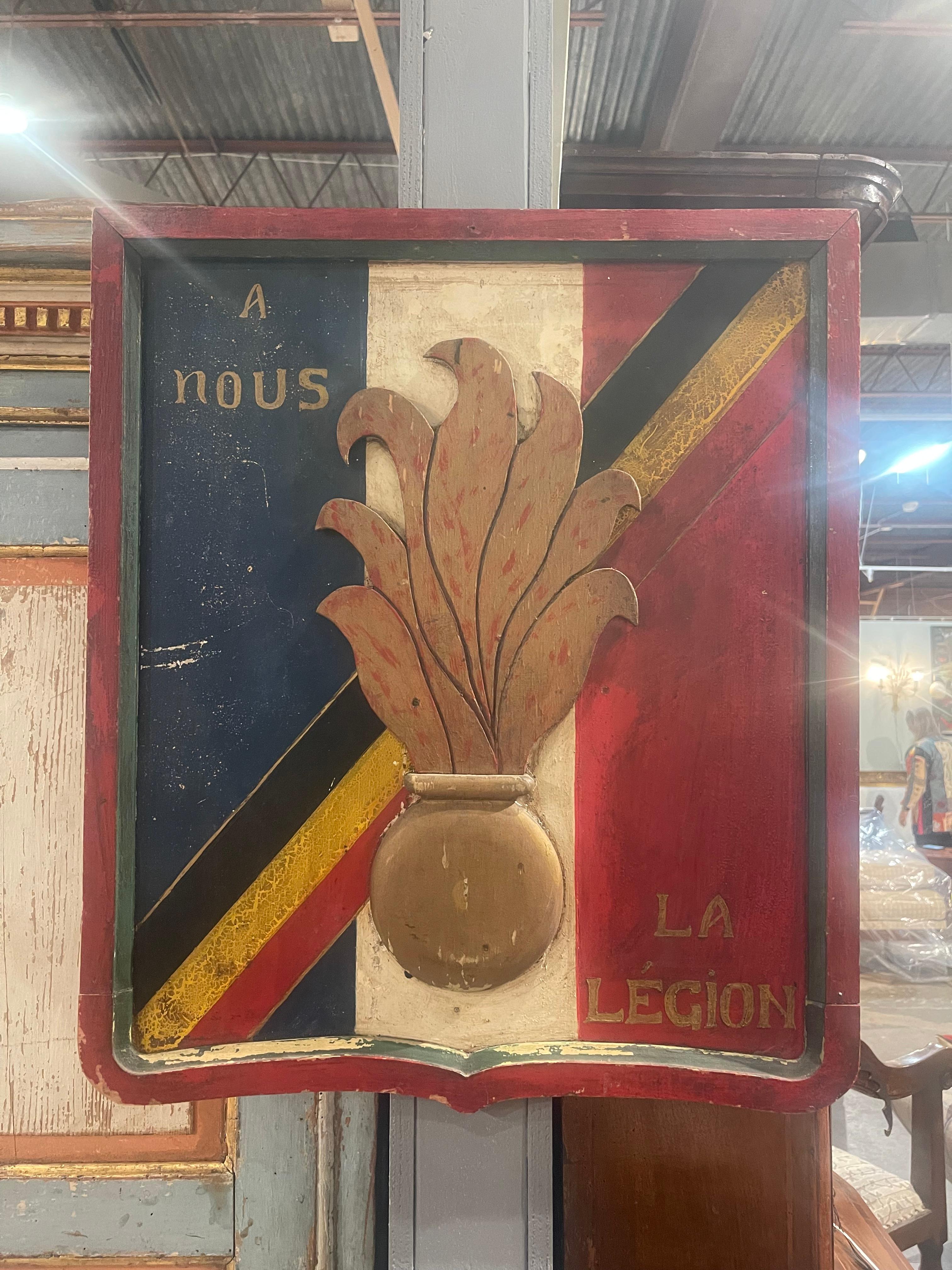Vintage Plaque der französischen Fremdenlegion, unterteilt in blaue, weiße und rote Abschnitte mit einem schwarz-gelben Streifen, der möglicherweise ein bestimmtes Regiment darstellt  oder Kampagnenunterscheidung.  In der Mitte ist das Relief einer
