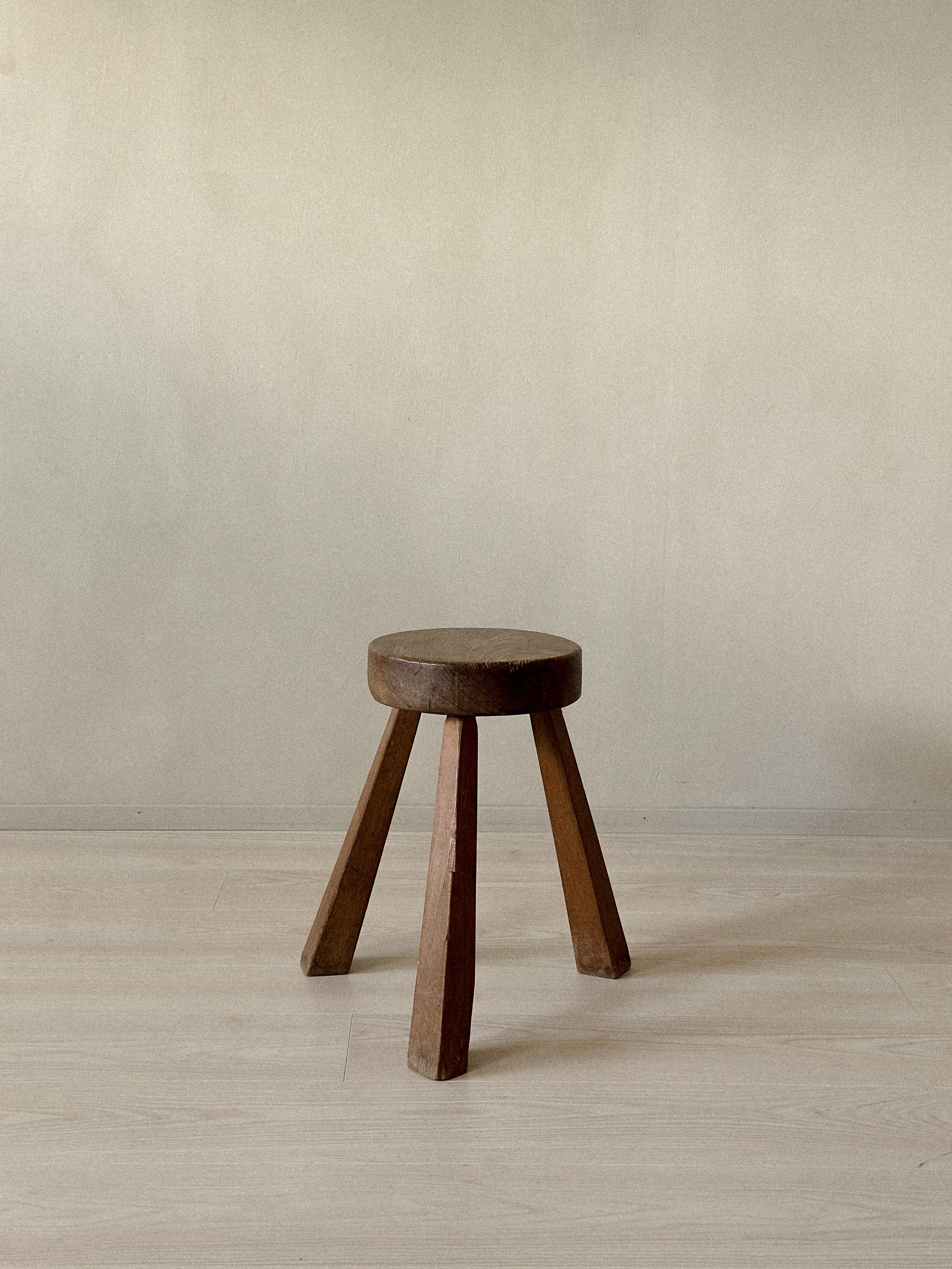 Sgabello da mungitura a tre gambe con seduta spessa e rotonda e gambe smussate. Struttura in legno massiccio con usura e patina visibili. Realizzato in Francia, intorno agli anni '60. Usura coerente con l'età e l'uso.