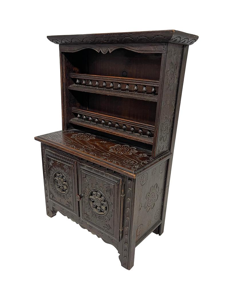 French miniature Breton Doll furniture, ca 1900

Oak wooden set with a hand-carved classic symbols of Breton design, including pinwheels, ball and stick, and incised flowers.  Brittany, France, circa 1900
The set consists of a cabinet with two doors