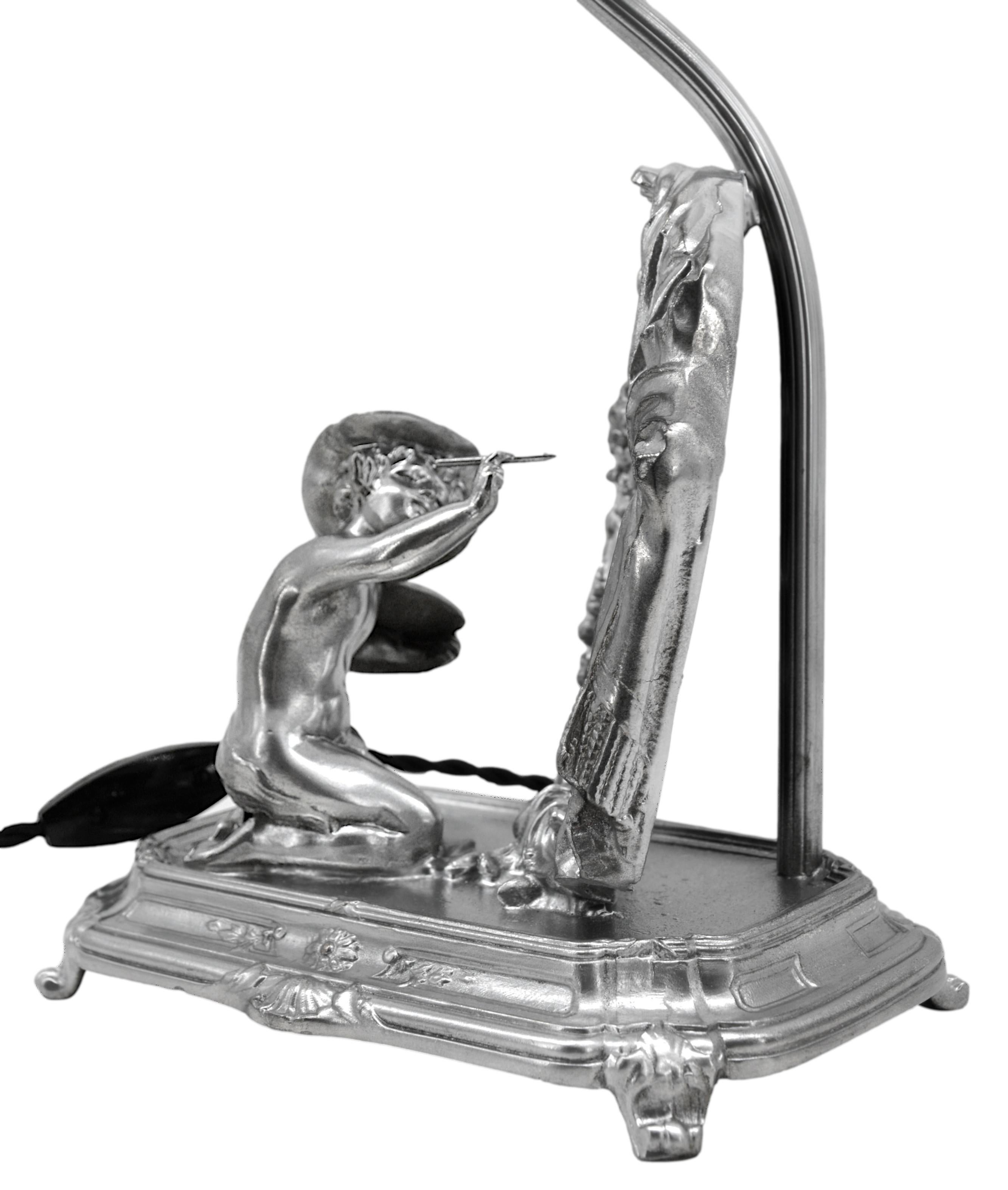 Lampe à poser qui fait également office de miroir représentant un tableau de putto. Spelter, tissu et miroir. France, vers 1900. L'abat-jour n'est pas d'époque. Mesures : Hauteur : 45,5 cm, largeur : 20,5 cm, profondeur : 14 cm. Très bon état. Livré