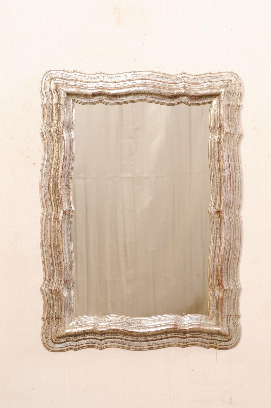 A French antiqued silver carved-wood mirror from the mid to later part of the 20th century. This vintage mirror from France has an overall rectangular shape with frame in a scalloped and stacked trim which gives this piece a beautifully rippling