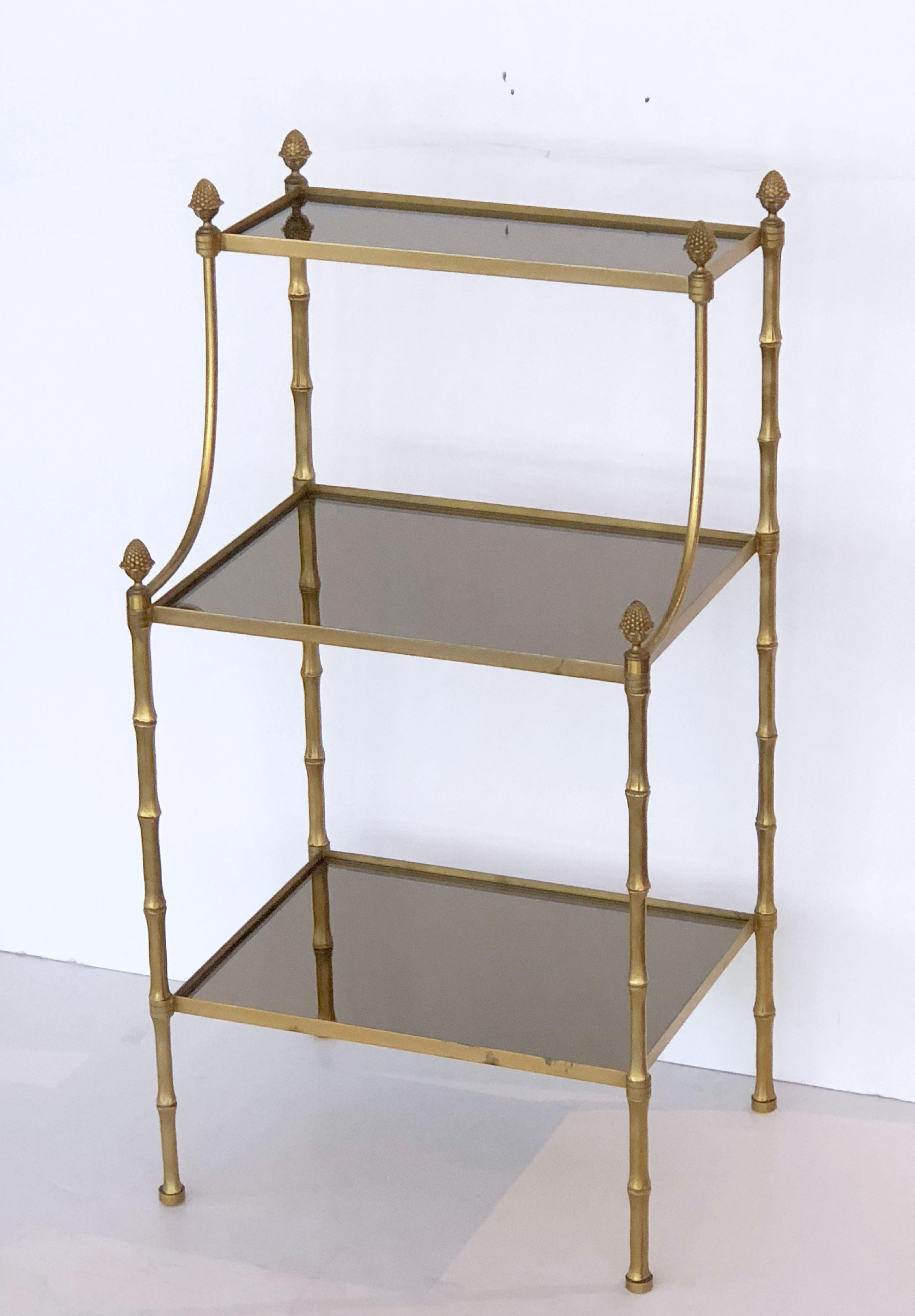 A handsome French étagère or shelf display of brass and tinted mirrored glass, featuring three tiers of rectangular mirrored glass in a faux bamboo brass frame, topped with finials.