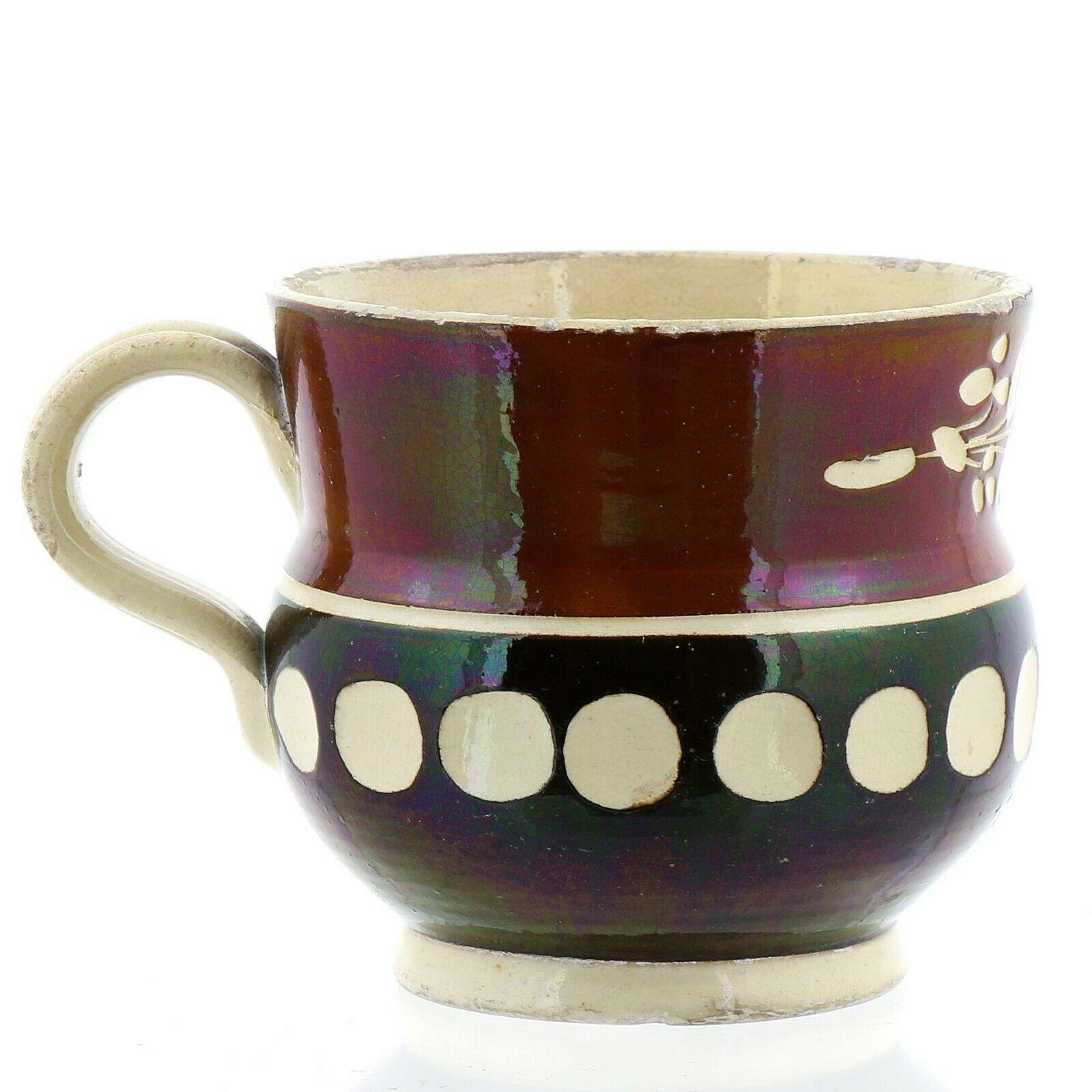 French Mocha Creamware mug, 1800-30

The mug is circular in form with an upper section in a plum color with white flowers and the lower slightly bulbous section in black with a band of white dots and with a plain cream-colored loop handle.