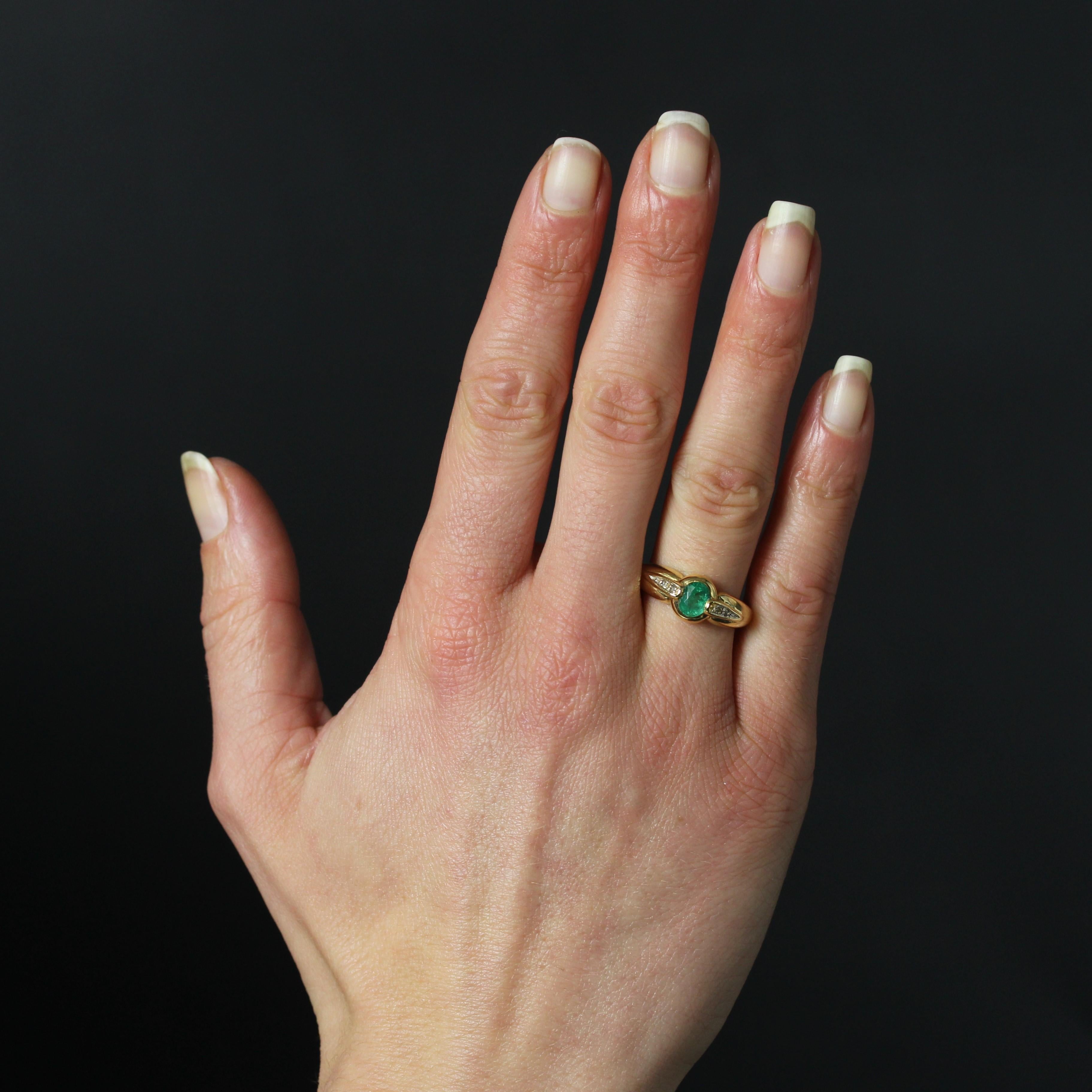 Ring in 18 karat yellow gold, eagle head hallmark.
The setting of this yellow gold ring features a wide band holding an oval emerald in the center. On either side of the central stone, two falling motifs are set in applique, each adorned with two