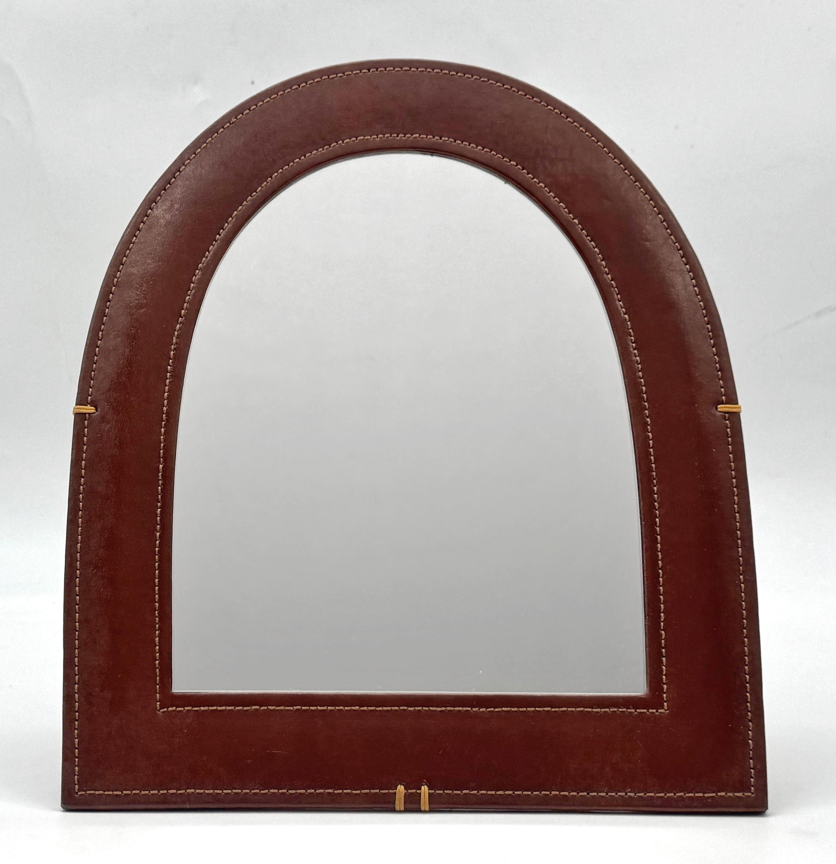 French Modern Leather-Wrapped Arched Tabletop Mirror, in the Style of Jacques Adnet, Late 20th C

A refined French Modern arched tabletop mirror, clad in warm brown leather with visible saddle stitching, evoking the timeless luxury of mid-century