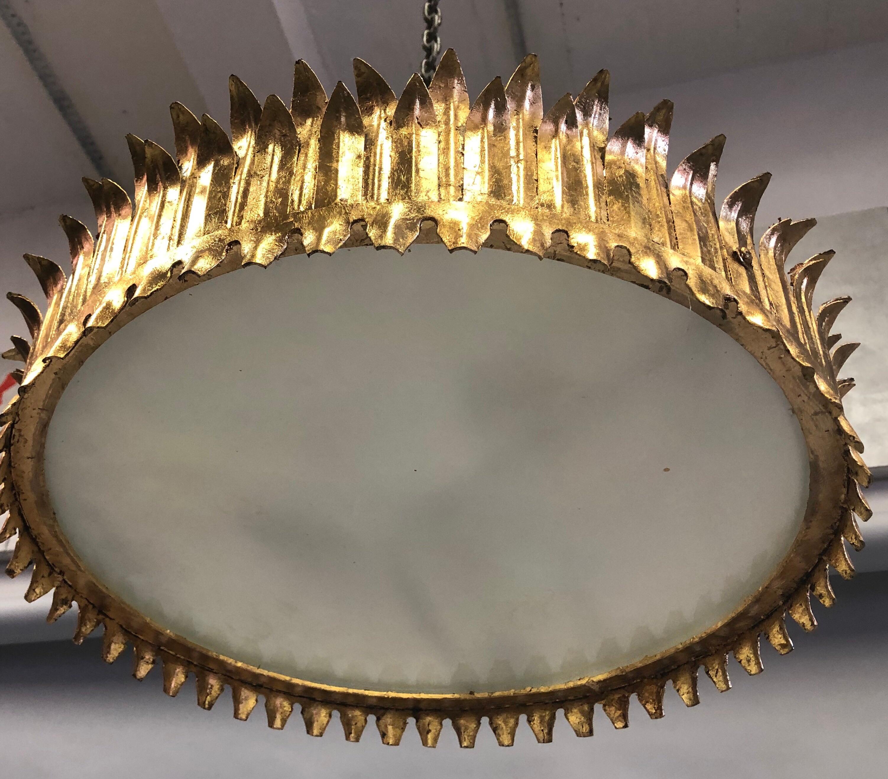 Elegant, dramatic large French Mid-Century Modern Neoclassical gilt iron fixture in the form of a crown or sunburst with a frosted glass center reflector. 
This piece is deeply influenced by the legendary French master iron worke of the 1940's,