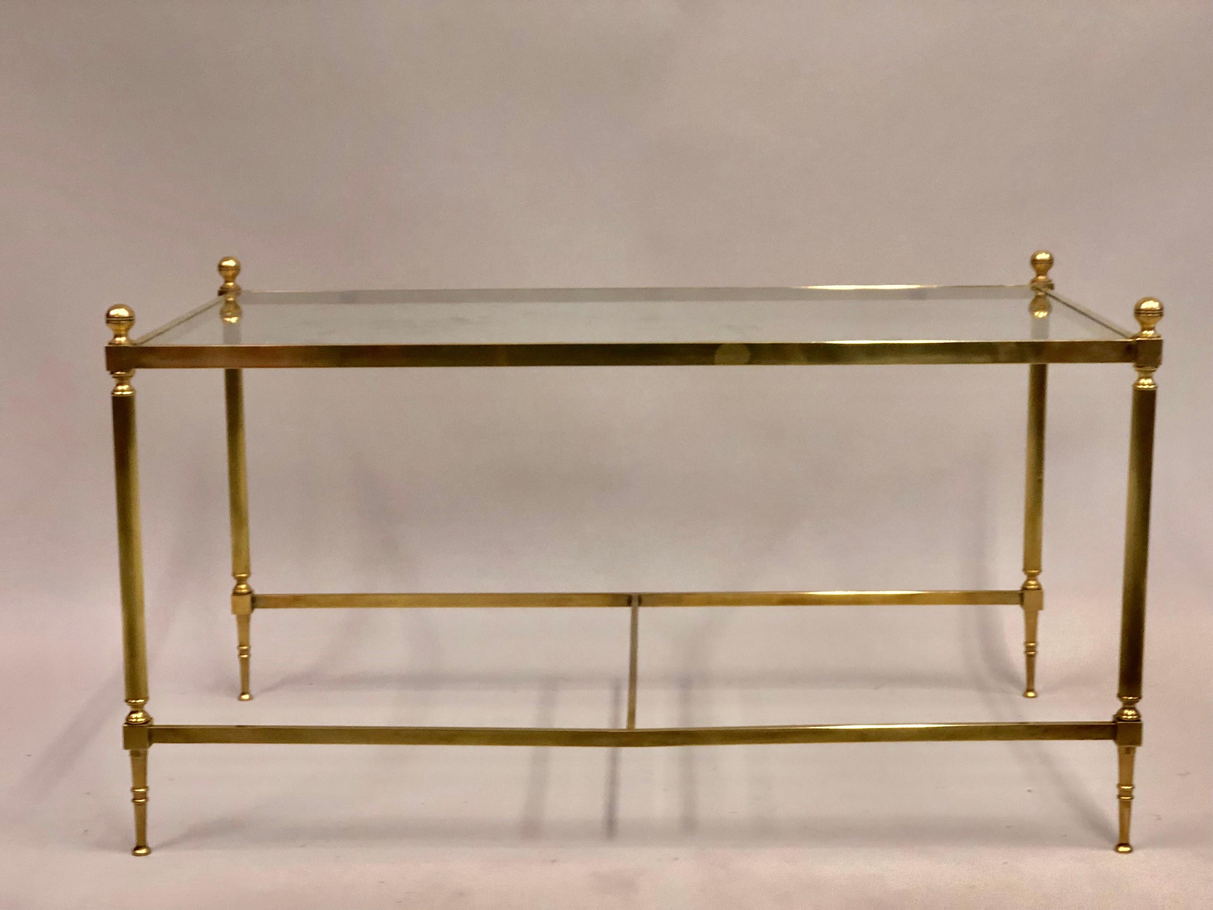 A delicate and refined French Mid-Century Modern Neoclassical cocktail table in solid brass with inset glass top by Maison Jansen circa 1950.  The table features sensuous fluted and tapered legs that terminate with thin pointed feet and dramatic