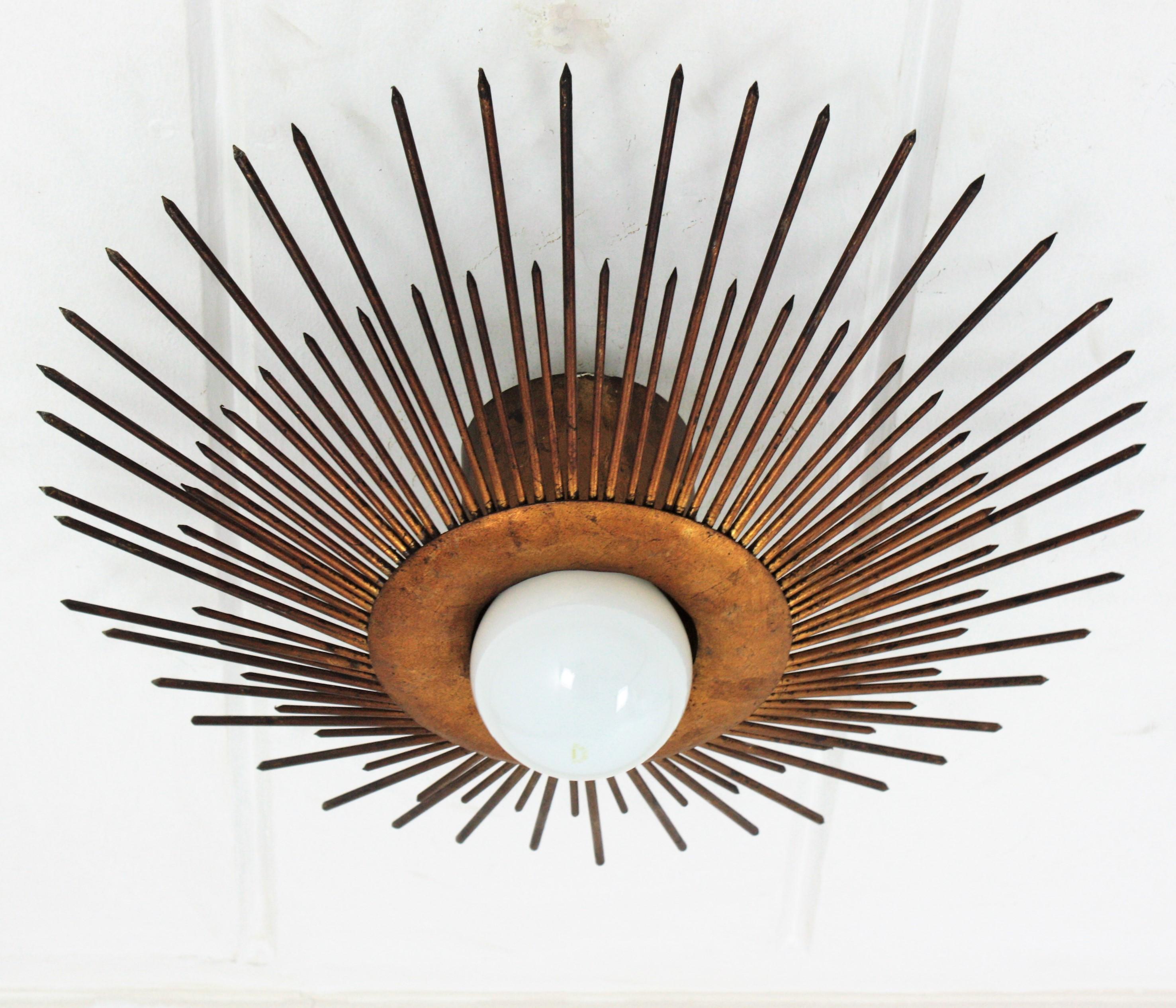 Large sunburst light fixture in gold leaf gilt iron, France, 1930s-1940s
French wrought iron bronze gilt large sunburst flush mount or pendant with nails or spikes frame.
A highly decorative sunburst ceiling light fixture with frontal light