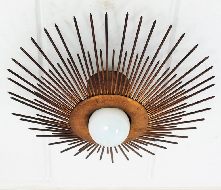 Large sunburst light fixture in gold leaf gilt iron, France, 1930s-1940s
French wrought iron bronze gilt large sunburst flush mount or pendant with nails or spikes frame.
A highly decorative sunburst ceiling light fixture with frontal light