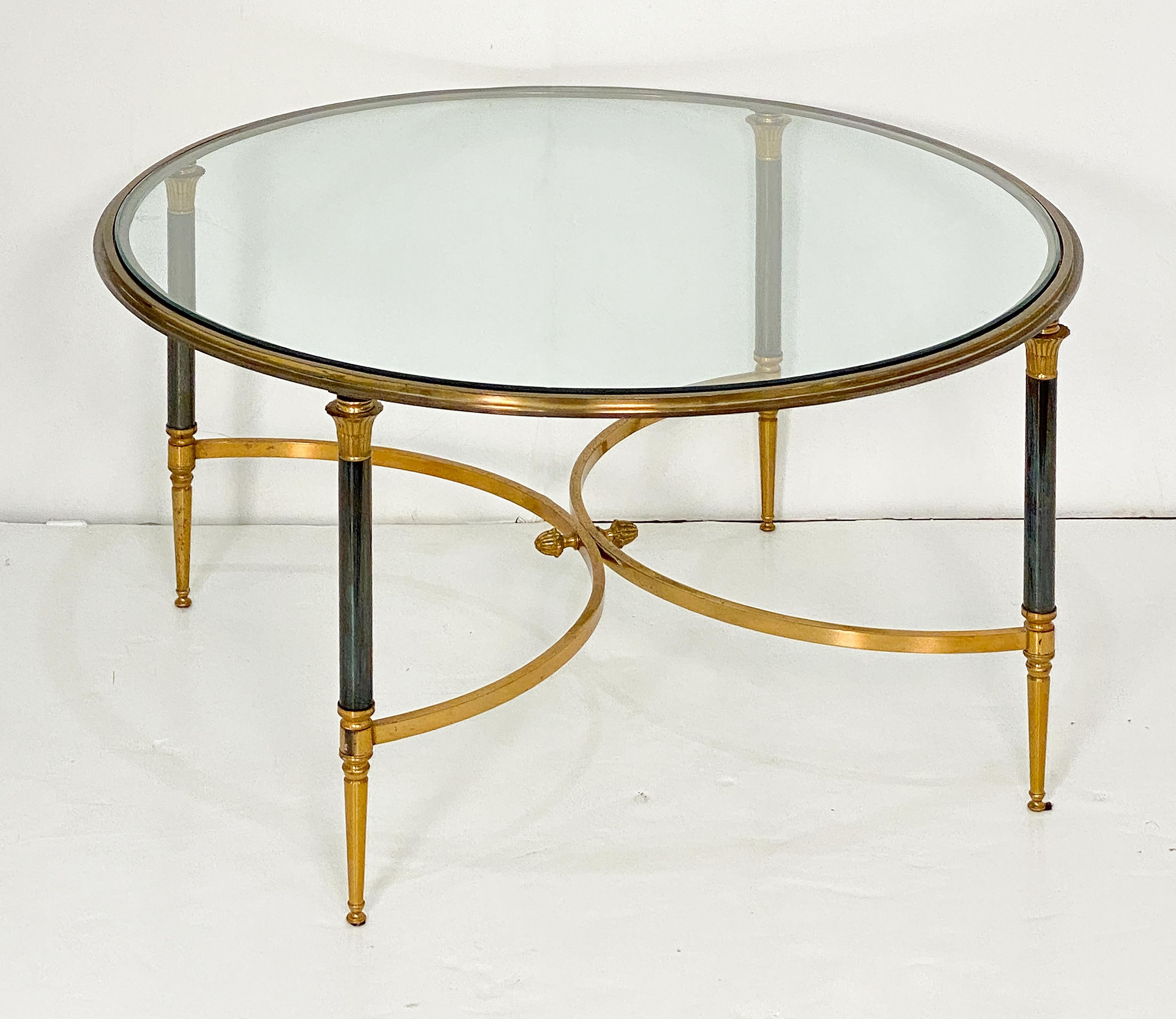 Table à cocktail, table basse ou table à café de style Maison Jansen, de forme circulaire, avec un plateau rond en verre reposant sur une structure en laiton avec des pieds fuselés et cannelés, chacun avec des tiges en métal brossé, adjoints à un