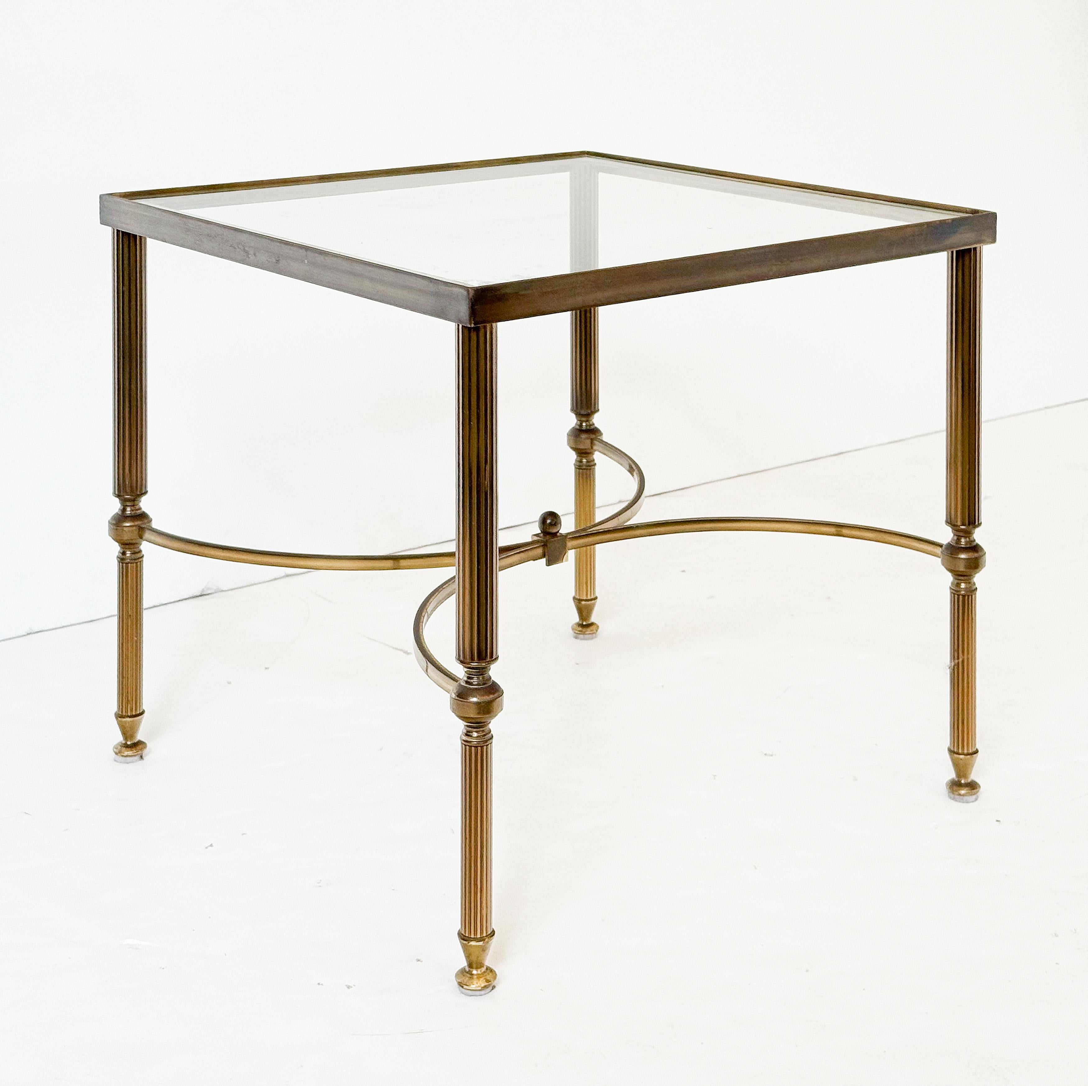 Table basse ou de cocktail de style moderne, avec un plateau carré en verre posé sur une structure en laiton aux pieds fuselés et cannelés, adjoints à un gracieux support en demi-lune.

Parfait pour une utilisation en tant que table basse.