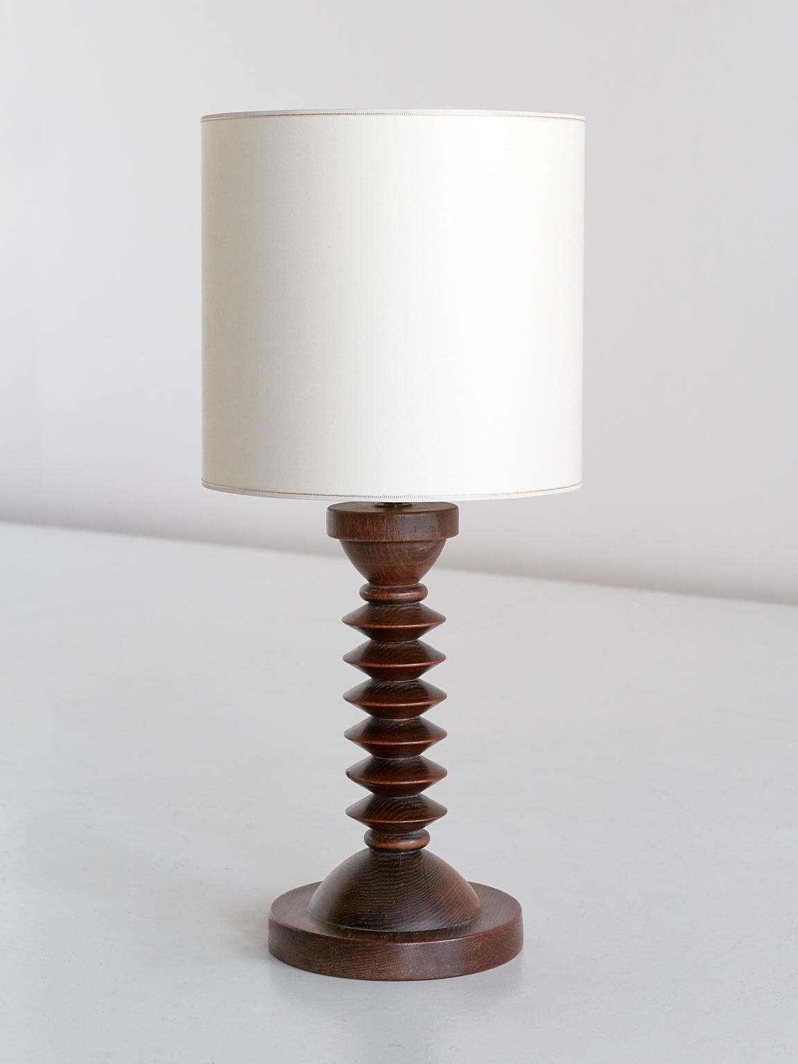 This rustic and elegant table lamp was produced in France in the 1950s. The lamp is made of dark stained oak wood and consists of a circular base and a carved stem in a stacked disc shape.
The new ivory shade distributes a soft and pleasant light.