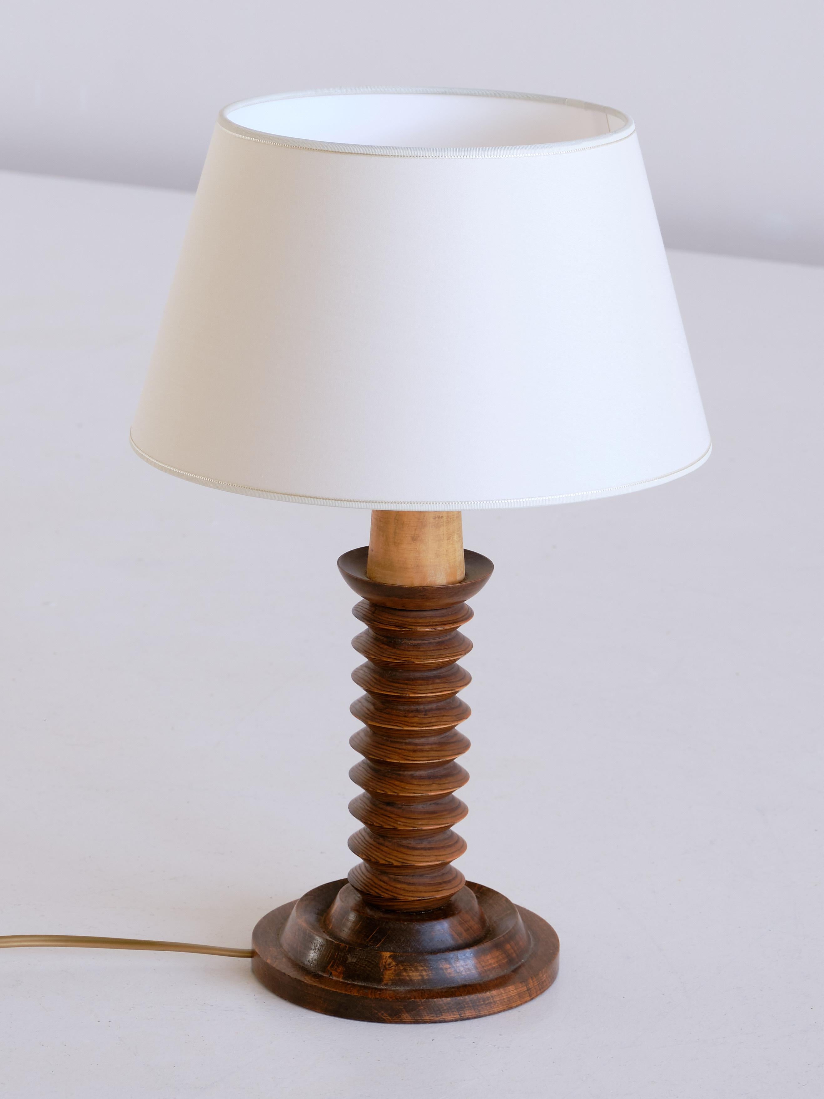 This rustic and elegant table lamp was produced in France in the 1950s. The lamp is made of dark stained oak wood and consists of a circular base and a carved stem in a stacked disc shape.
The new ivory shade distributes a soft and pleasant light.