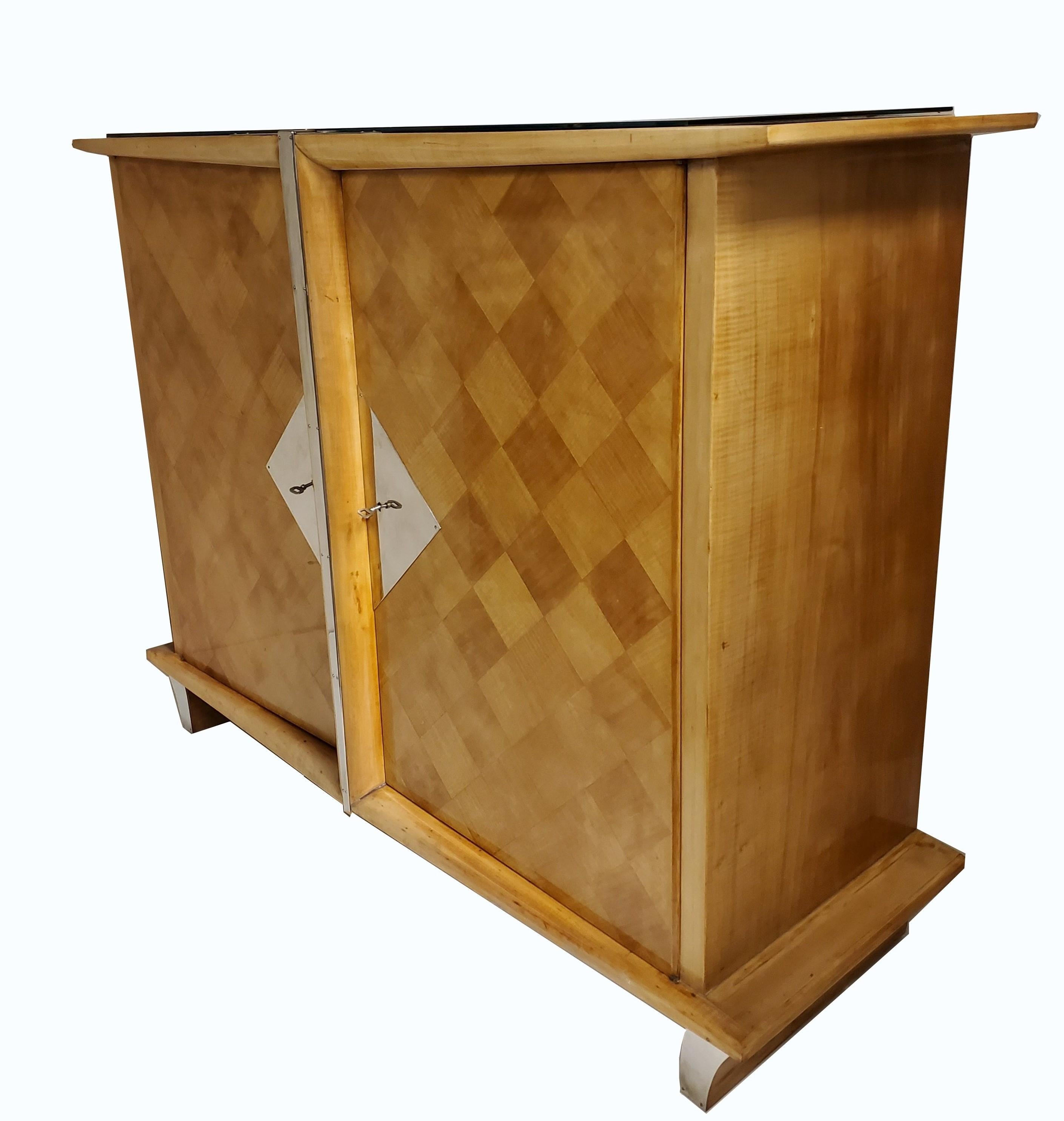 Armoire haute en bois de sycomore, haute et polyvalente. 
Sa façade en marqueterie géométrique ajoute une touche d'élégance avec des motifs de losanges et de cubes. Ce meuble sculptural est orné d'une moulure conique artistique qui se prolonge