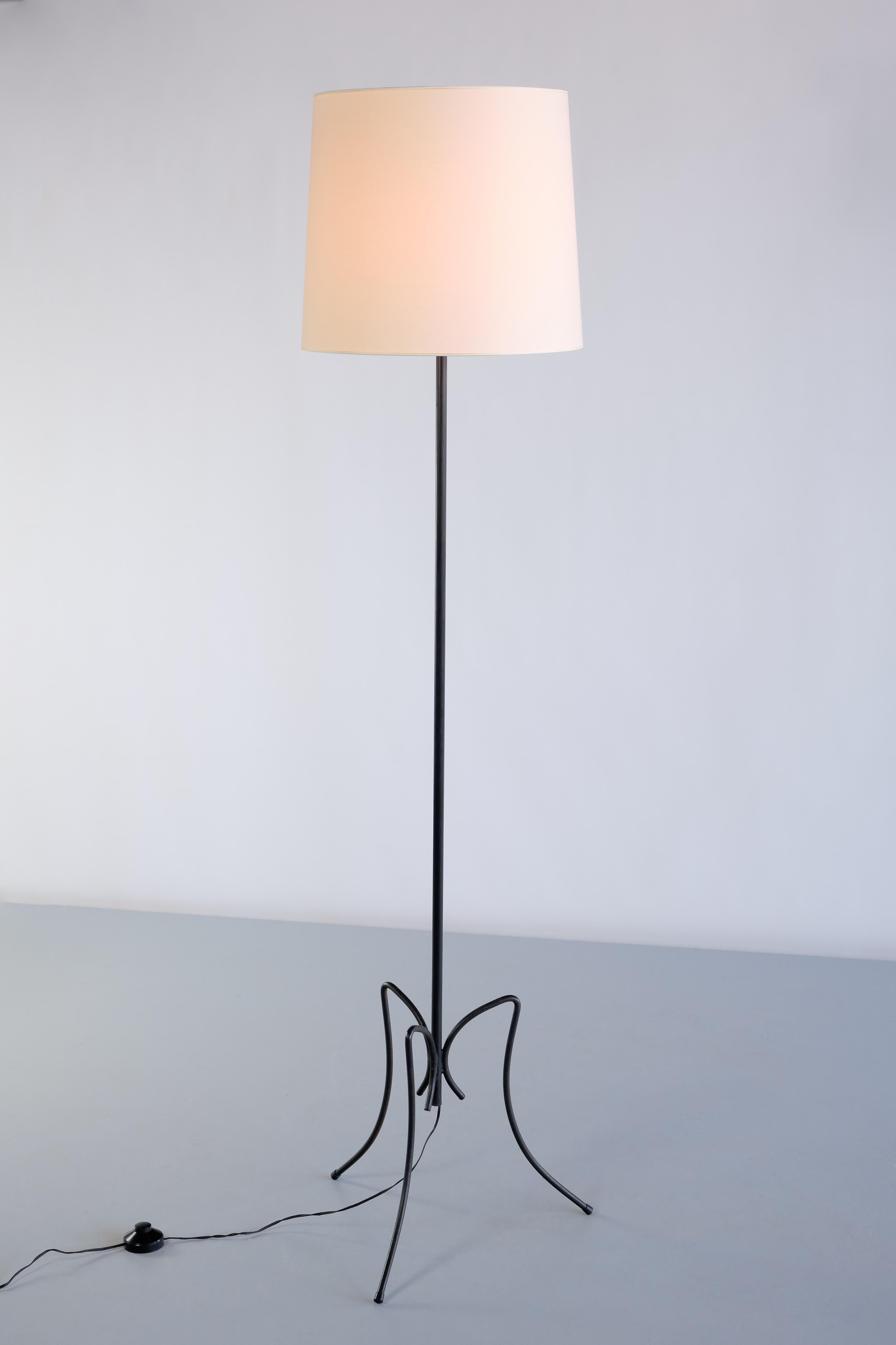 This striking floor lamp was produced in France in the early 1950s. The lamp consists of a three legged base and thin stem, all in black lacquered iron. The iron outward bending legs in a curved movement give the lamp a delicate and elegant