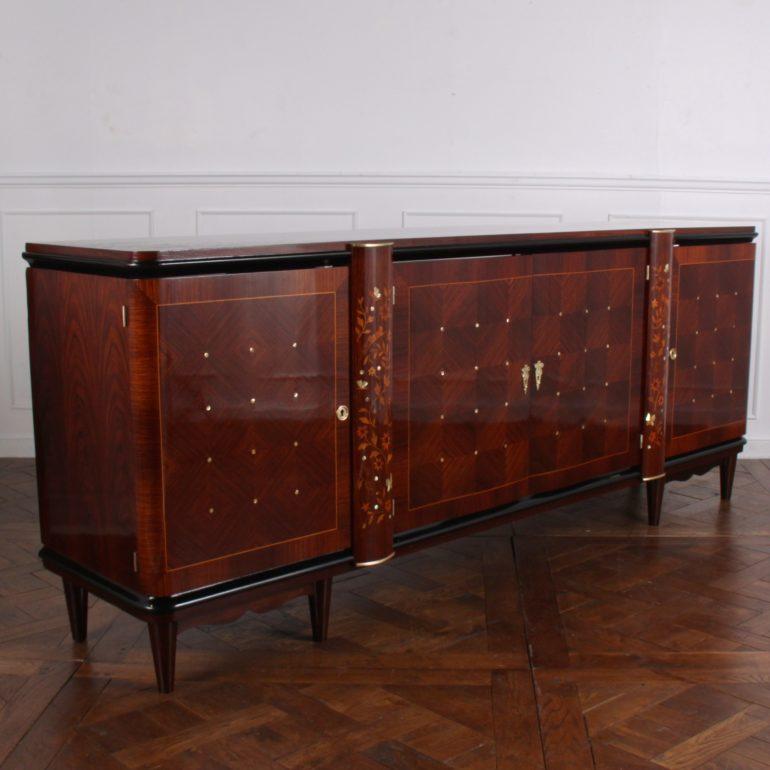 A French, mid-20th century, four-door buffet in Macassar ebony, the doors with geometric book-matched veneer punctuated with mother of pearl, the two central doors flanked by pilasters richly inlaid with birds, flowers, and butterflies in exotic
