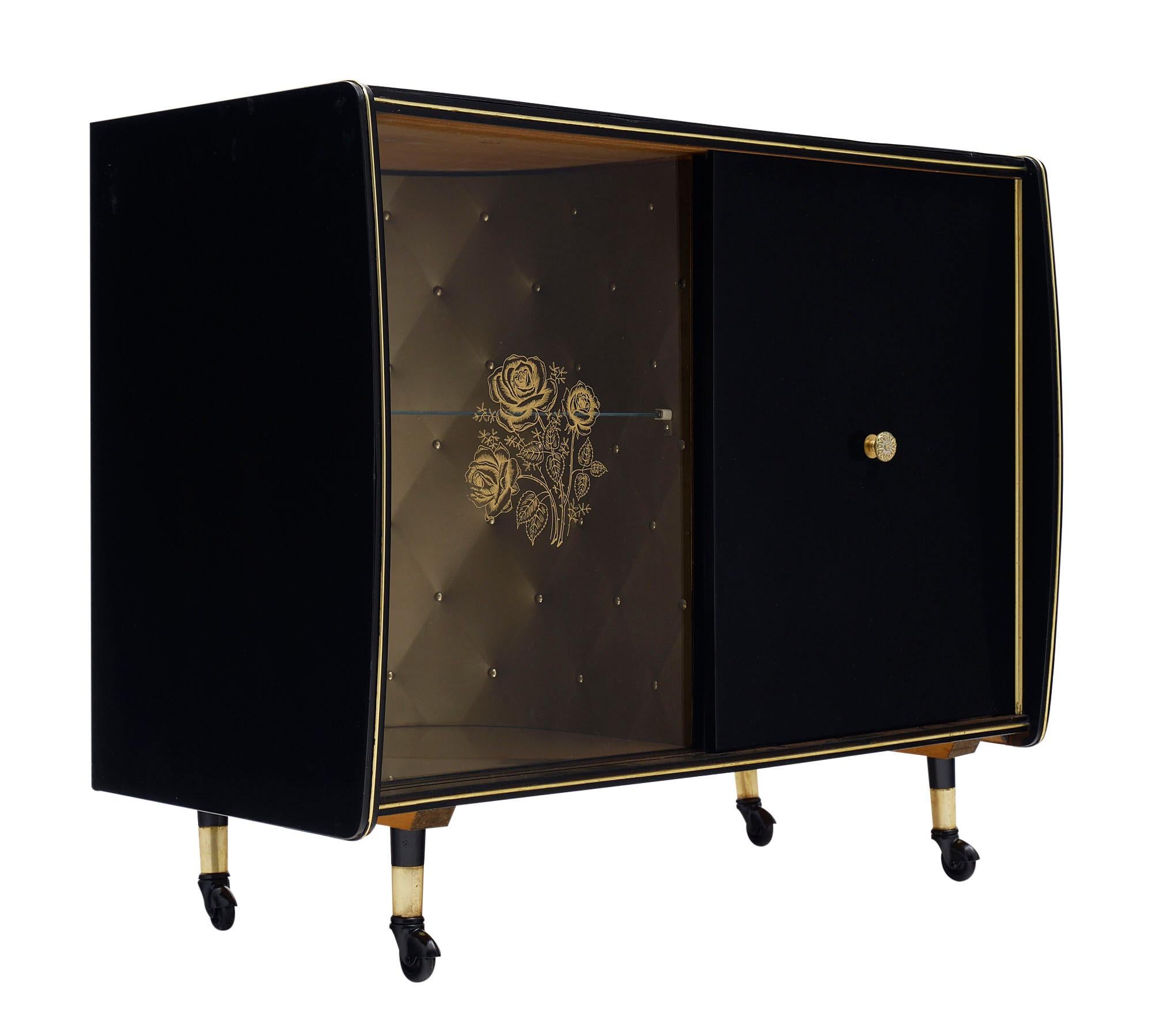 Bar cart; French; from the Modernist era with sliding wooden and glass doors. The glass door has a gold leafed floral motif. The cabinet is on wheels and is the top is veneered with textured black glass and trimmed with gilt brass. There are