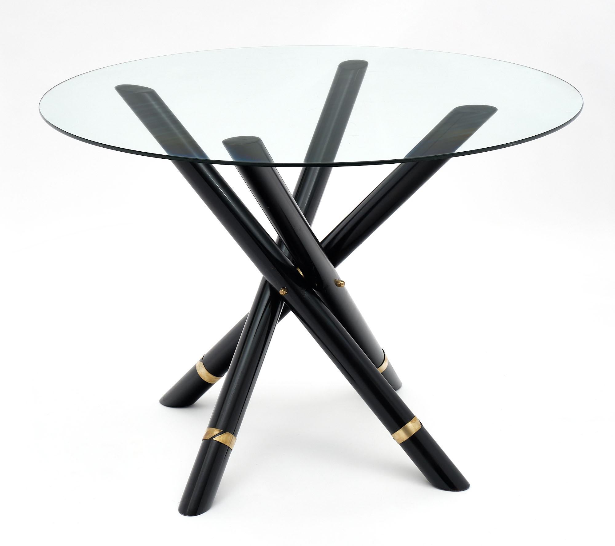 Round dining table or gueridon from France featuring a foldable base with four black lacquered steel tubes enhanced with a gilt brass ring. The top is glass.