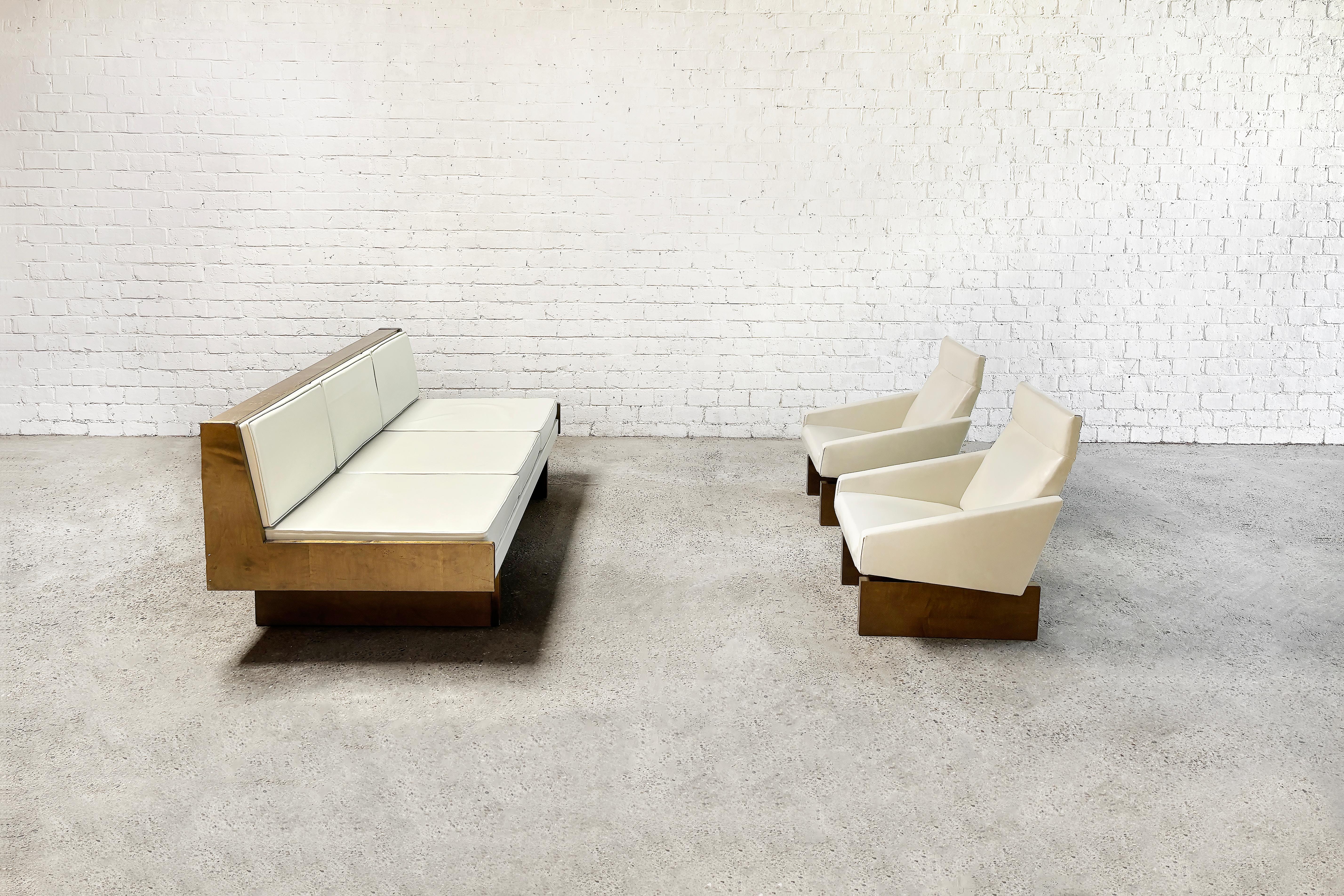 Introducing an impressive French modernist living room set from the 1950s, featuring a versatile three-seater sofa that converts into a day bed, accompanied by two lounge chairs. Both the sofa and chairs retain their original white eco-leather