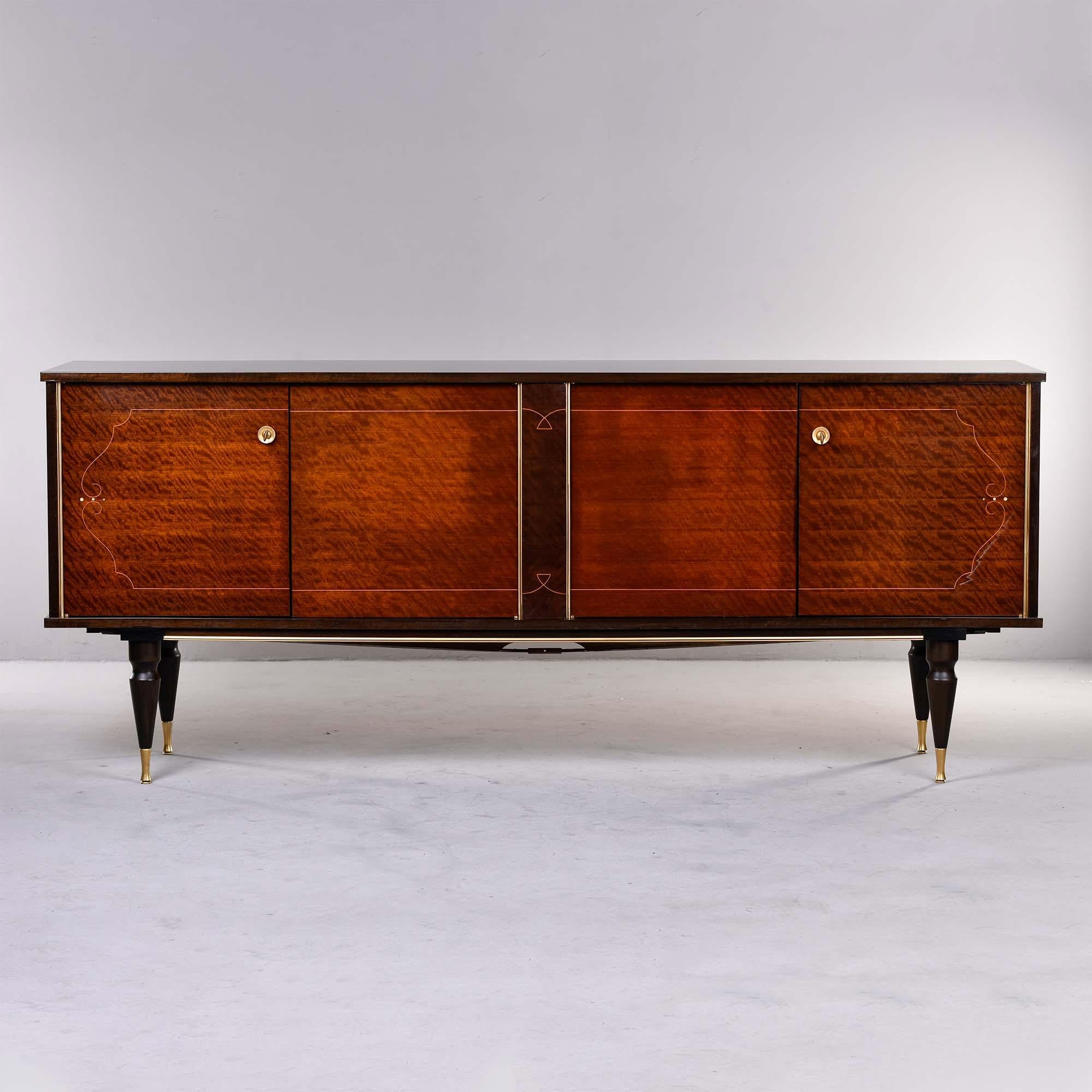 Circa 1940s French buffet or credenza in mahogany with contrasting legs, accents and brass trim. Cabinets on both sides have functional locks. Both storage compartments have a single internal shelf and one side has three small drawers as well.