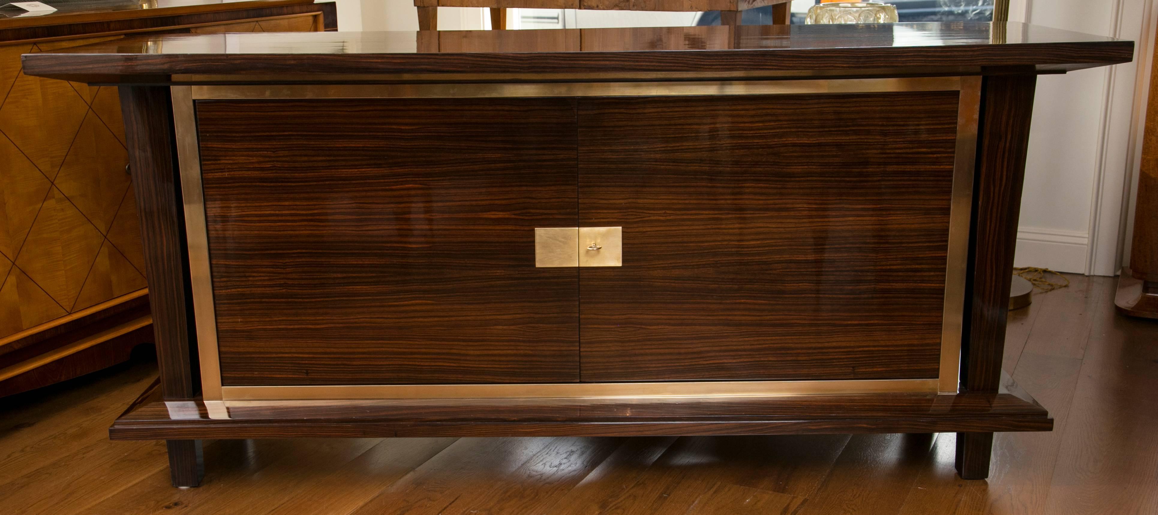 Streamline two-door sideboard flanked by graduated side columns in an elegant rosewood veneer adorned with brass inlay and hardware, interior veneered in sycamore, extraordinary quality, French polished.
Origin
France
Creation