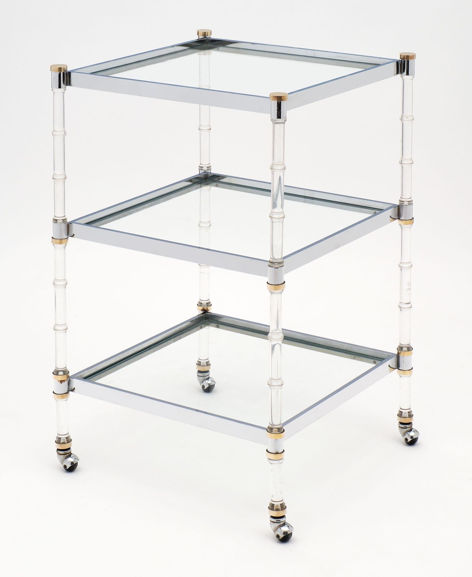 Three tiered modernist French bar cart with unique details and original wheels. This piece is made of Lucite, chrome and brass. We loved the strong structure in great condition and the flawless combination of materials. The shelves themselves are