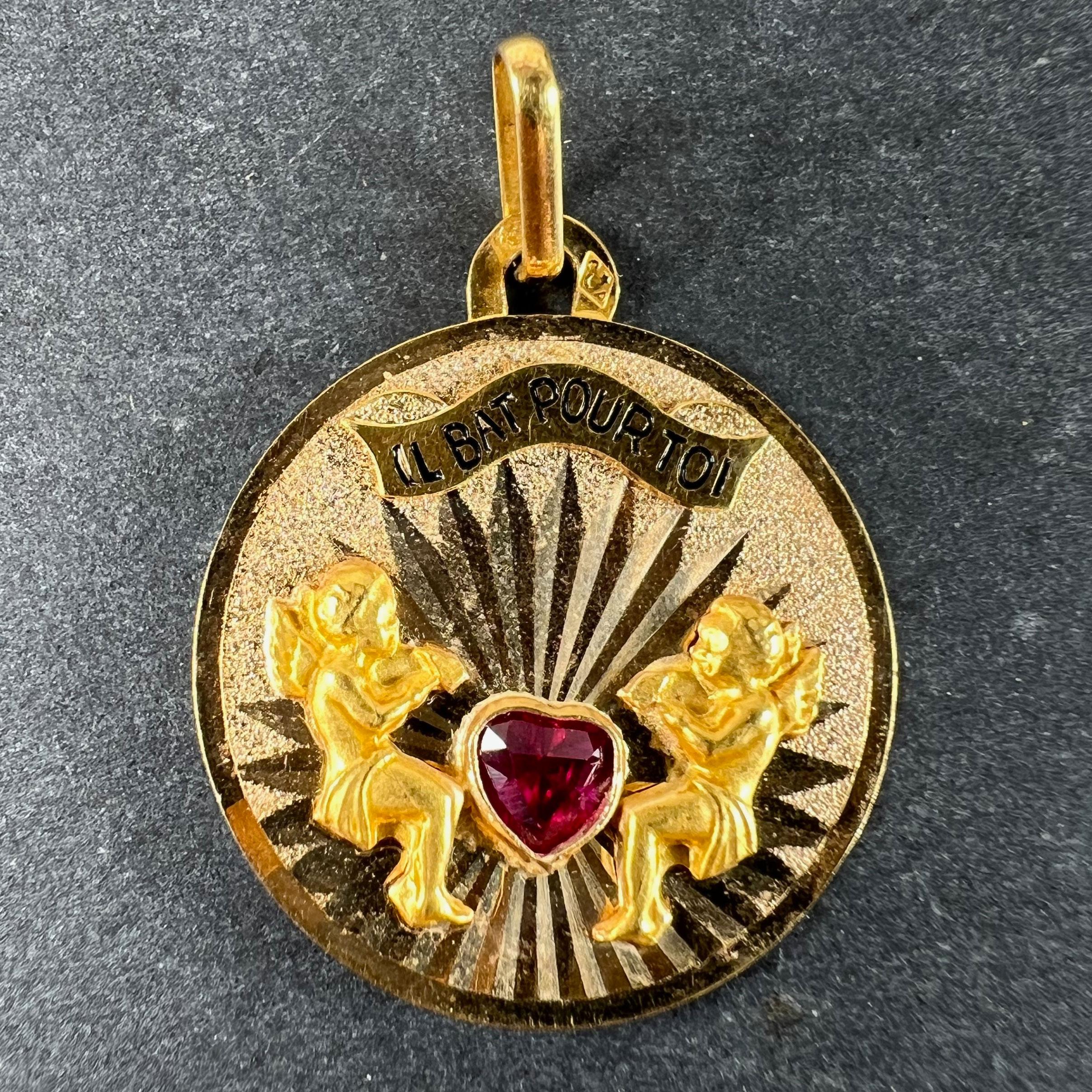 Pendentif à breloque rond en or 18 carats (18K) conçu comme un fond gravé et texturé de rayons de soleil rayonnant à partir d'un cœur d'amour en rubis synthétique, avec deux figures de cupidon en or jaune avec des marteaux en position pour battre le