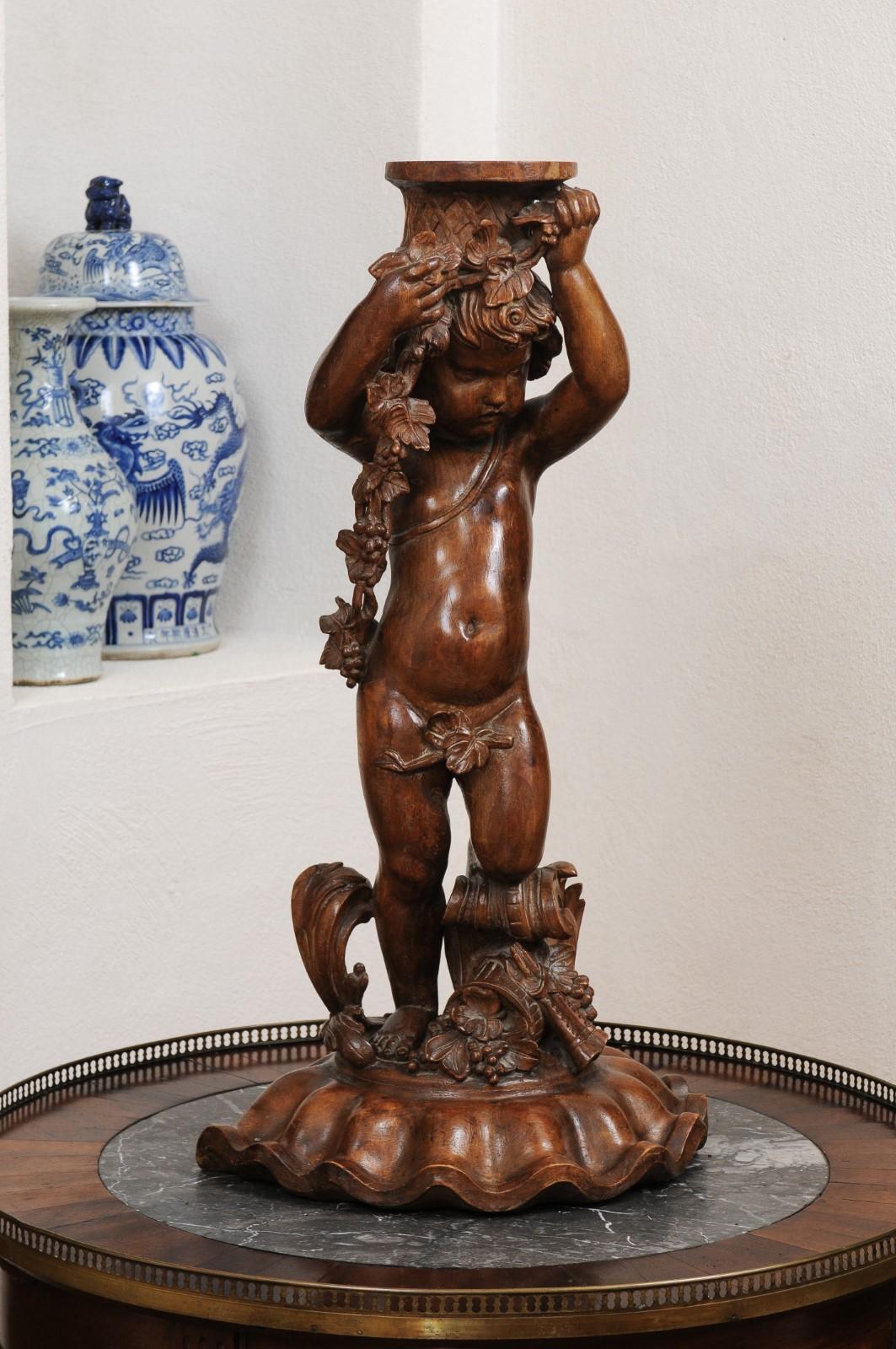 A French Napoléon III period walnut carved putto sculpture from the mid 19th century, with grapes, flowers and the double flute. Created in France during the third quarter of the 19th century, this carved walnut sculpture depicts a putto draped with