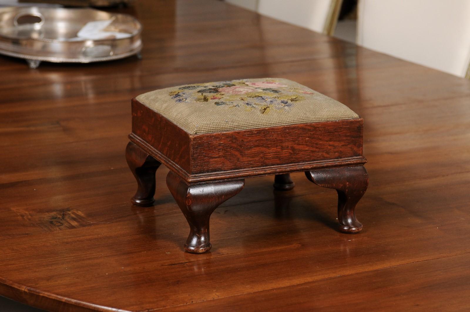 A French Napoléon III period petite footstool from the late 19th century, with floral needlepoint upholstery. Created in France during the third quarter of the 19th century, this petite footstool features a square top covered with a needlepoint