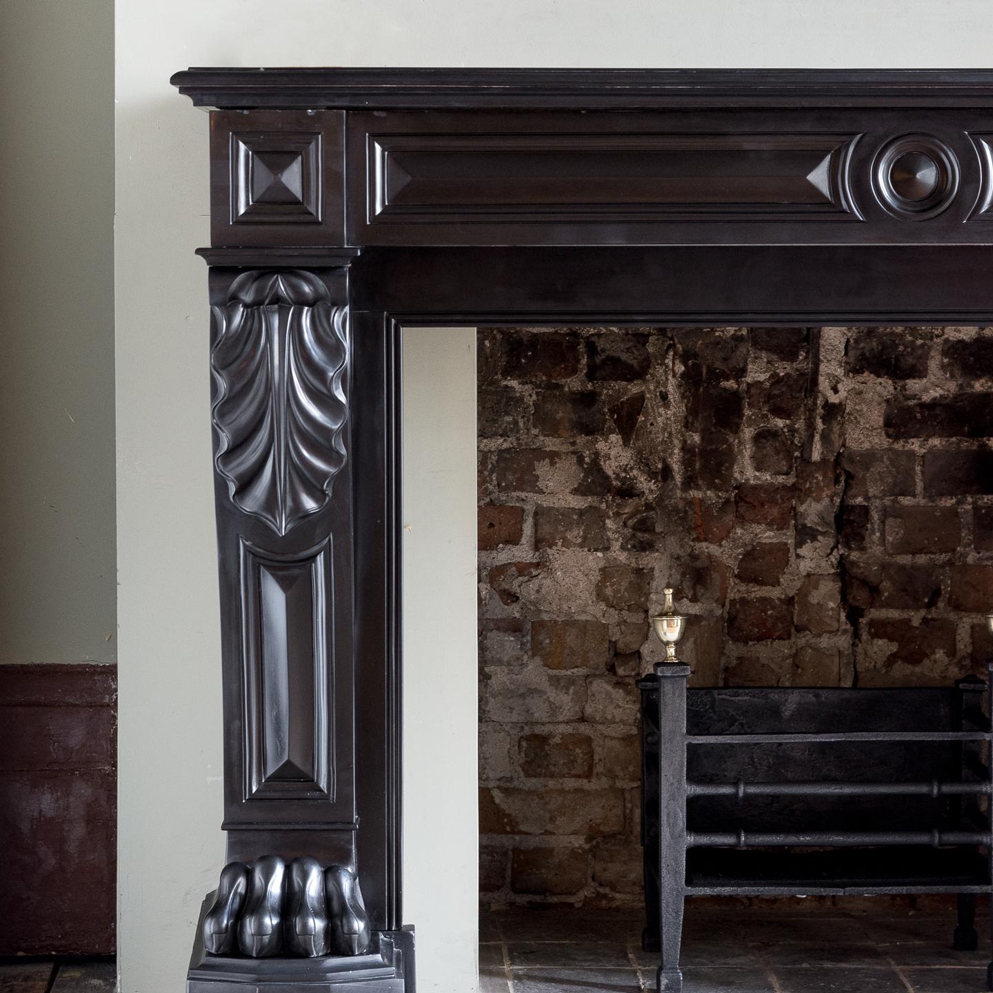 A French Napoleon III Belgian Black marble chimneypiece, the deep moulded shelf above paneled frieze centred by roundel, the console jambs terminating in richly carved lion's paw feet, on faceted footblocks.

Measures: Opening width 104 cm x 79.5
