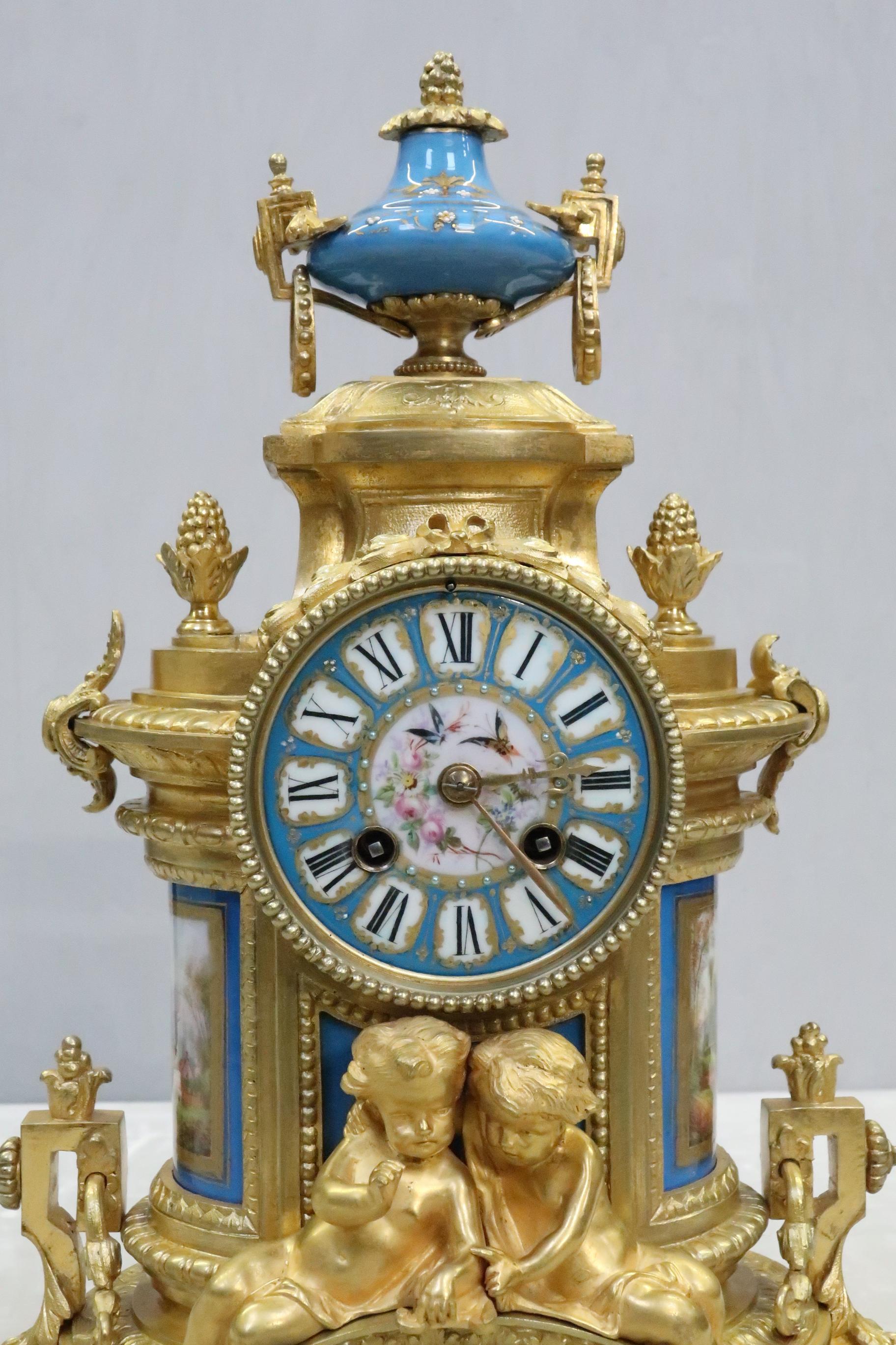 An impressive French Napoleon III bronze gilt mantel clock with decorative mouldings, beaded detail, and leaf design throughout adorned with putti and surmounted with finals and porcelain urn. The clock has inset blue sevre style porcelain panels