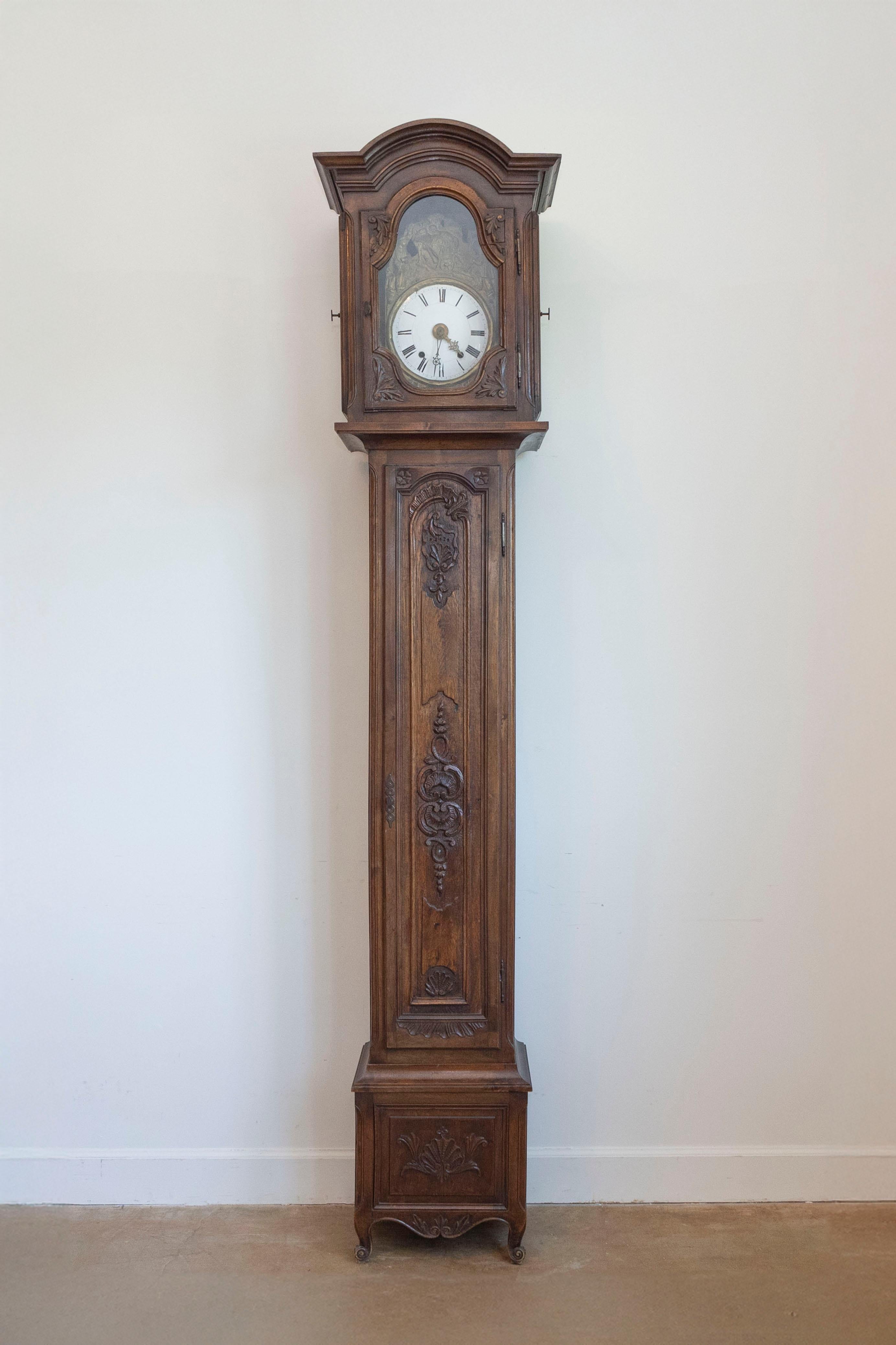 A French Napoléon III period carved walnut antique long case clock from the mid-19th century, with bonnet top, farming scene and scrolling motifs. Created in France at the beginning of Emperor Napoléon III's reign, this walnut grandfather clock