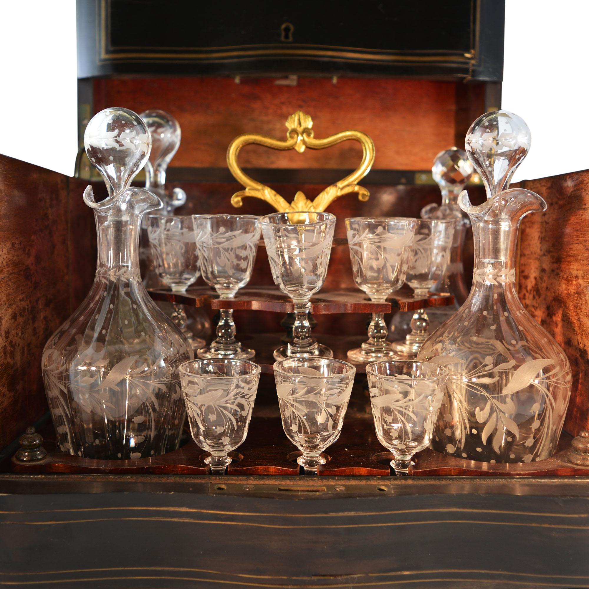 Liquor cave in brass inlaid ebony wood with rosewood interior. Front and top of the box sides are decorated with brass inlay. The tantalus set contains a removable wooden inset with brass lift handle. Includes hand cut and engraved crystal decanters