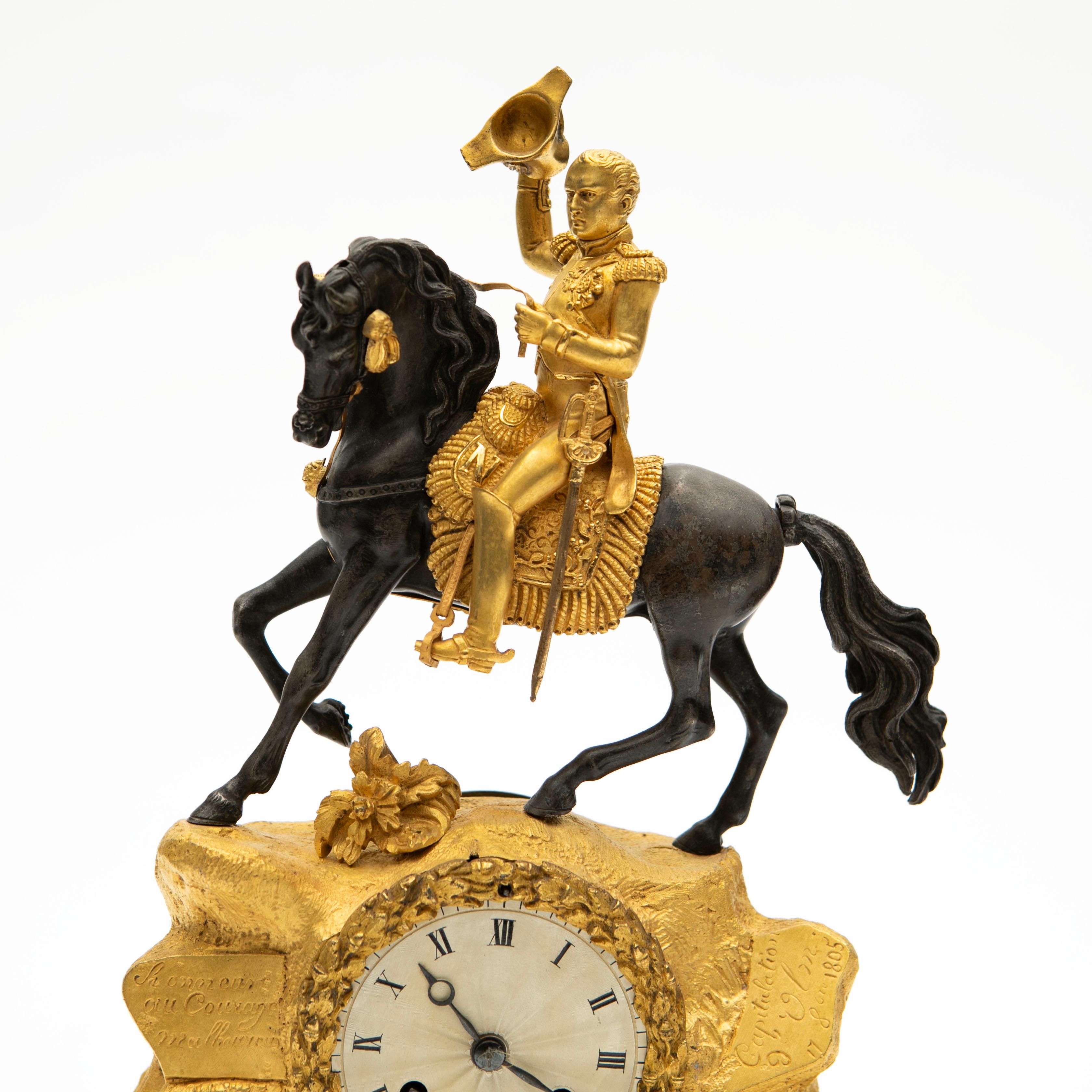French pendulum fireplace mantel clock in chiseled gilded and patinated bronze. The upper part with rock formation depicting an equestrian statue of Emperor Napoleon I on horseback over the Alps at the Great St Bernard Pass raising his hat in a