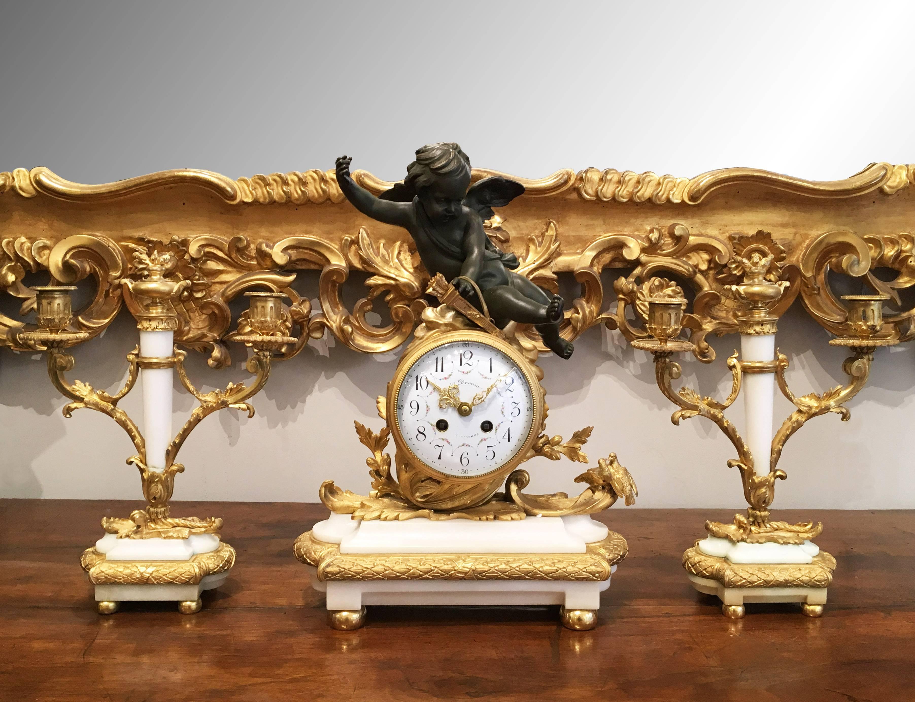 A superb French Napoleon III gilt bronze and white marble set clock set comprising of a pair of two branch candelabras and a mantel clock. The clock is adorned by two love-birds and a patinated bronze cupid and presents a white enamelled dial