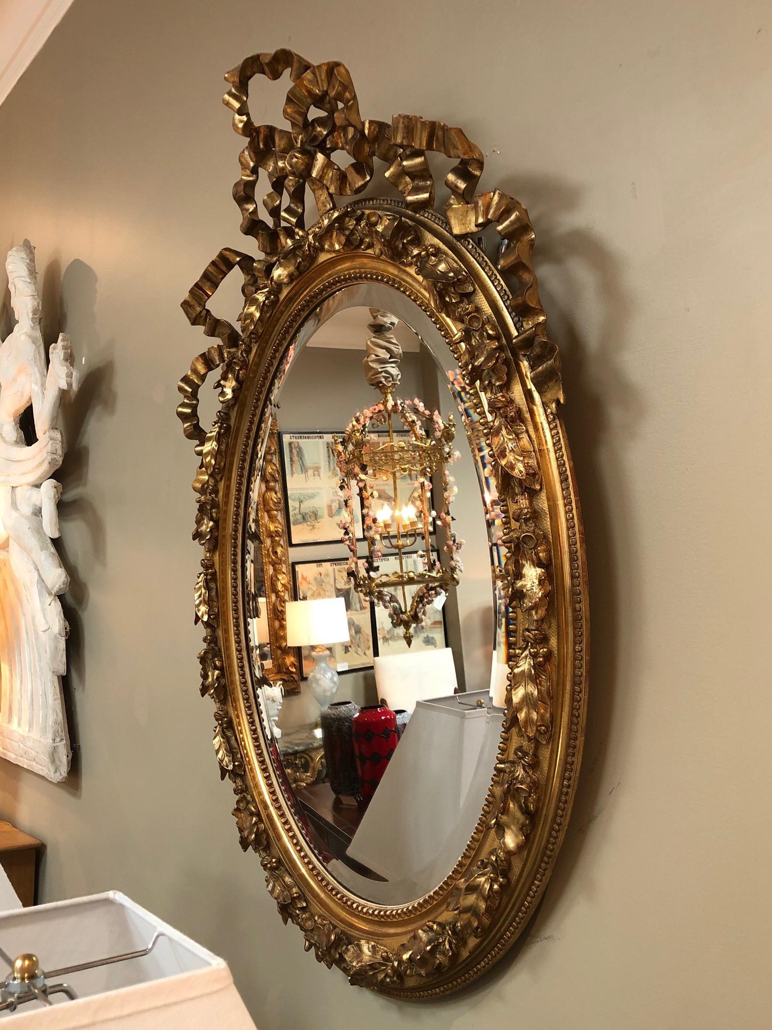 The well-executed mirror with flourishing ribbon crest above an oval frame adorned with oak and laurel leaf border; surrounding the original beveled mirror.