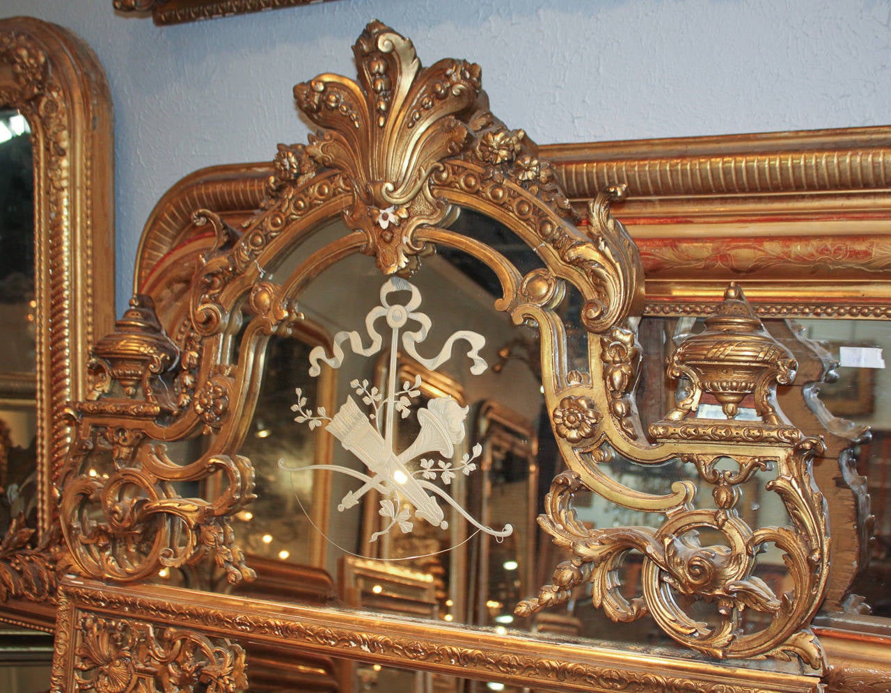 Stunning giltwood French Napoleon III mirror with elaborate mirrored cartouche. Having image of torch, quiver and bow in mirrored glass, large capped finials, and beveled glass. A sensational piece wonderful for numerous designs!