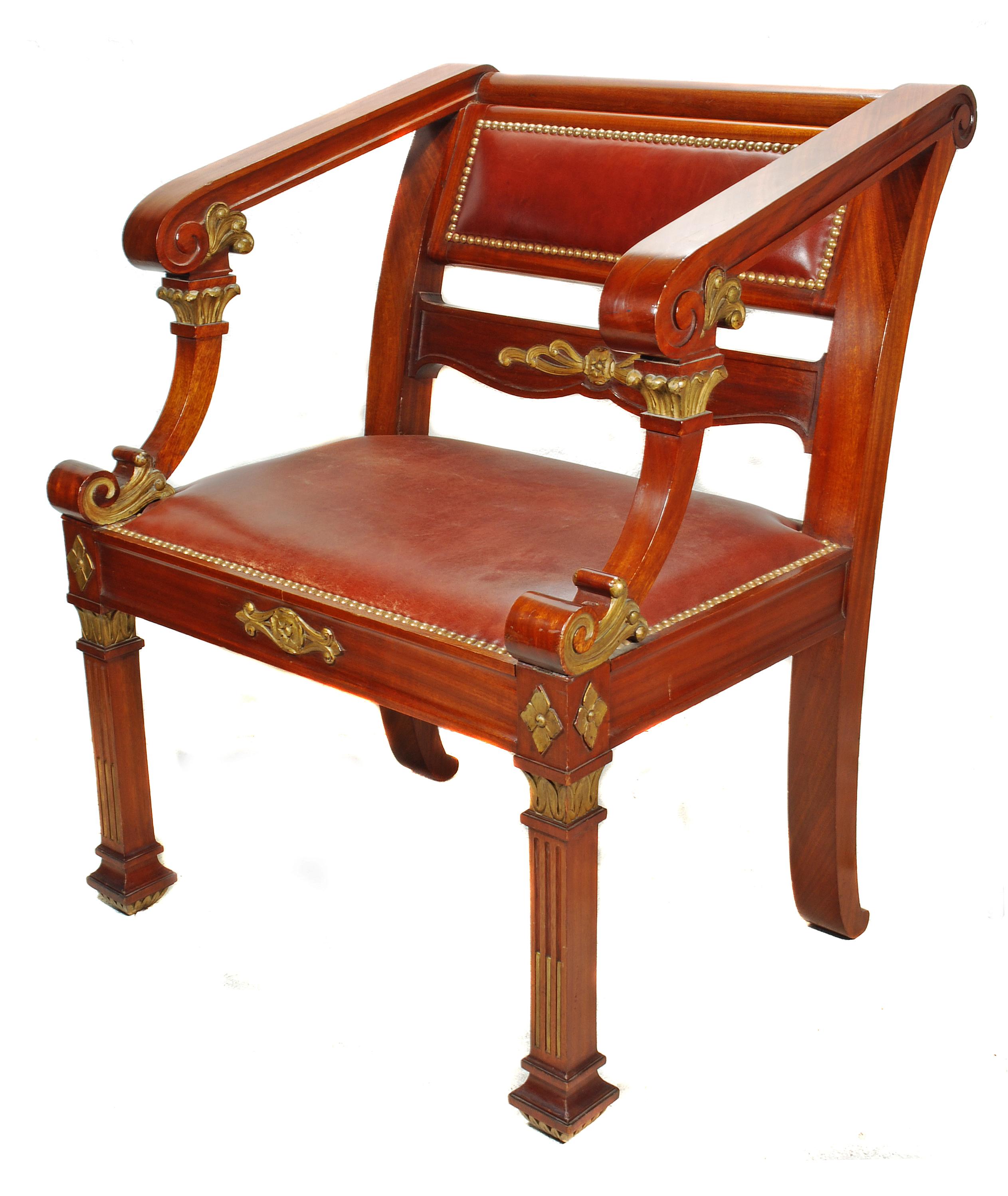 A large Napoleon III desk chair in mahogany, with original tan leather seat and backrest, lined with brass studwork, France, circa 1890. The frame with gilt foliate detailing to the backrest and apron, with a flower topping the front square legs,