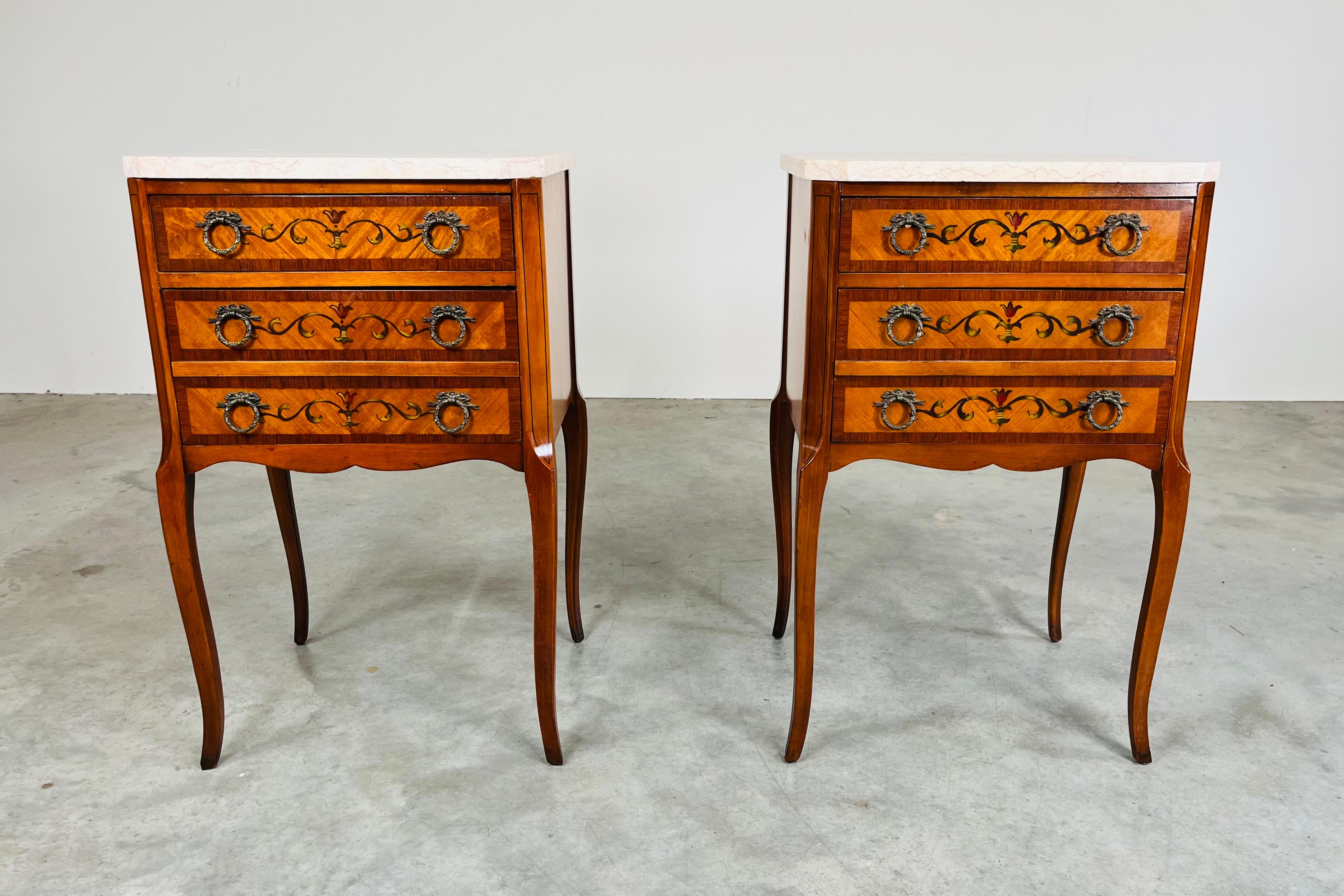 A beautiful pair of walnut nightstands having kingwood marquetry embellishments, hand painted drawer front details and Rosalia marble tops. Each nightstand has two drawers. One shallow top drawer over a deep double bottom drawer having hand carved