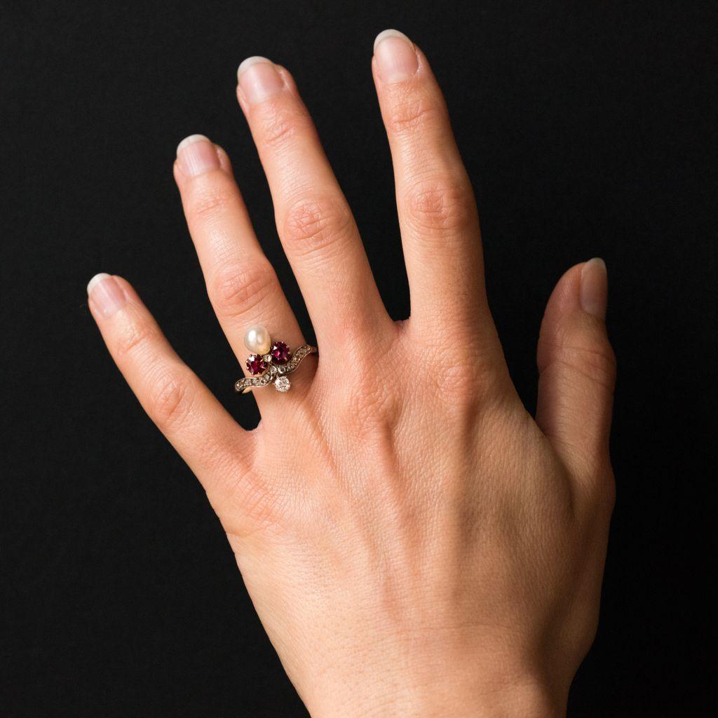 Ring in 18 karat yellow gold.
This gorgeous ‘Duchess’ antique ring is claw set with 2 rubies separated by a small bezel set rose- cut diamond with a natural baroque pearl above. An antique brilliant- cut diamond is set just at the beginning of the