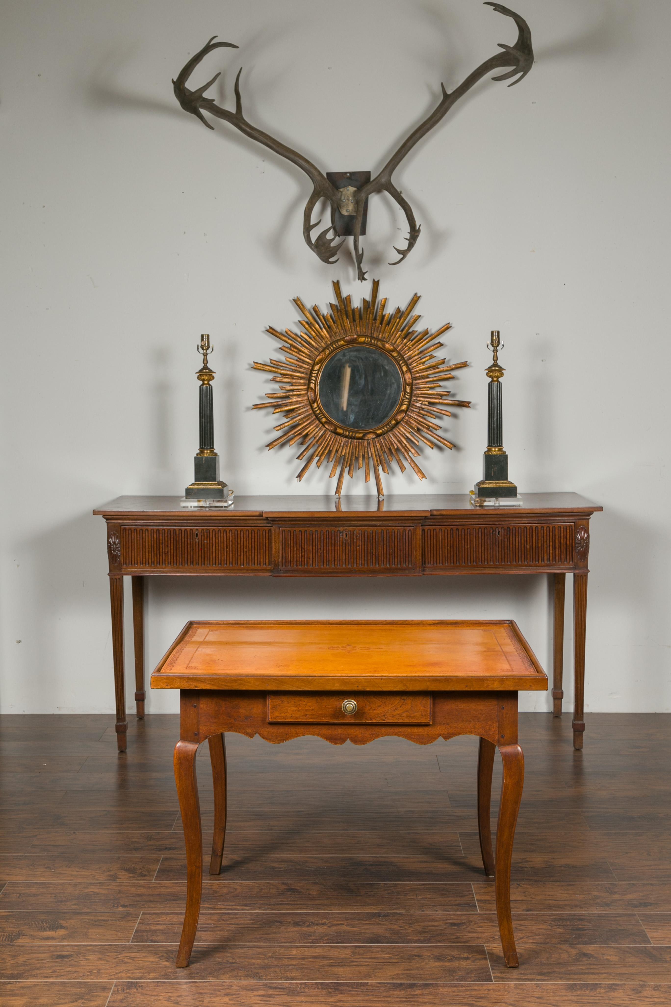 A French Napoleon III period walnut table from the mid-19th century, with leather top and single drawer. Created in France during the 1850s, this walnut table features a rectangular tooled leather top sitting above an apron scalloped on all sides