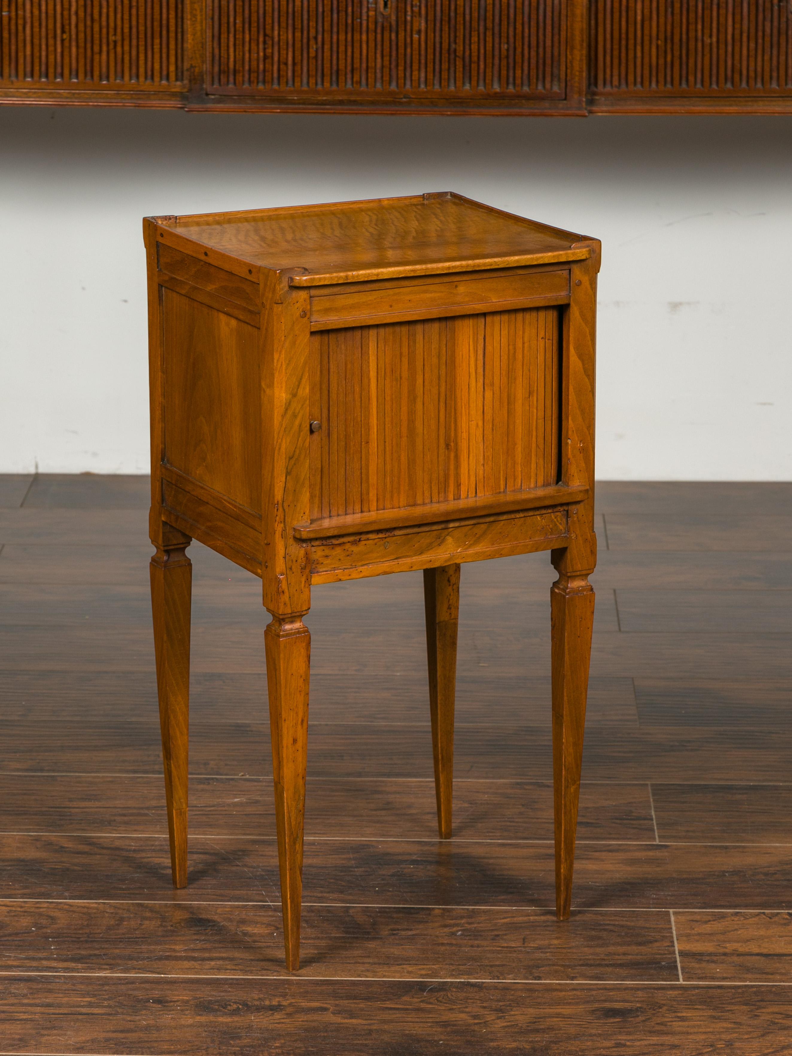 A French Napoleon III period walnut bedside table from the late 19th century, with tambour door and tapered legs. Born in France during the third quarter of the 19th century, this walnut side table features a rectangular top with slightly raised