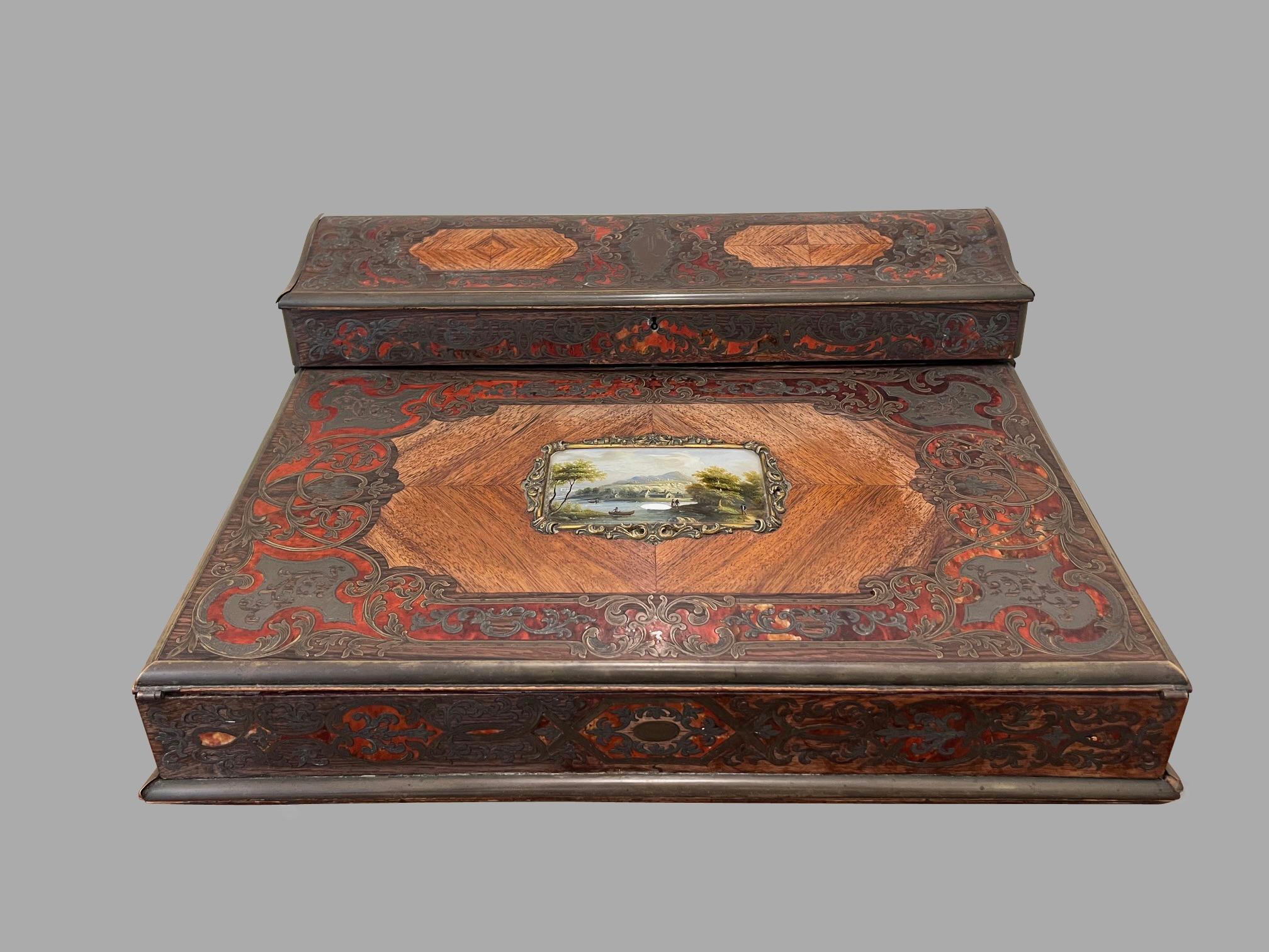 A very pretty French Napoleon III period brass inlaid rosewood and kingwood lap desk of fine quality. This portable writing desk is centered by a beautifully painted landscape scene. The fall opens to a velvet lined writing surface and the