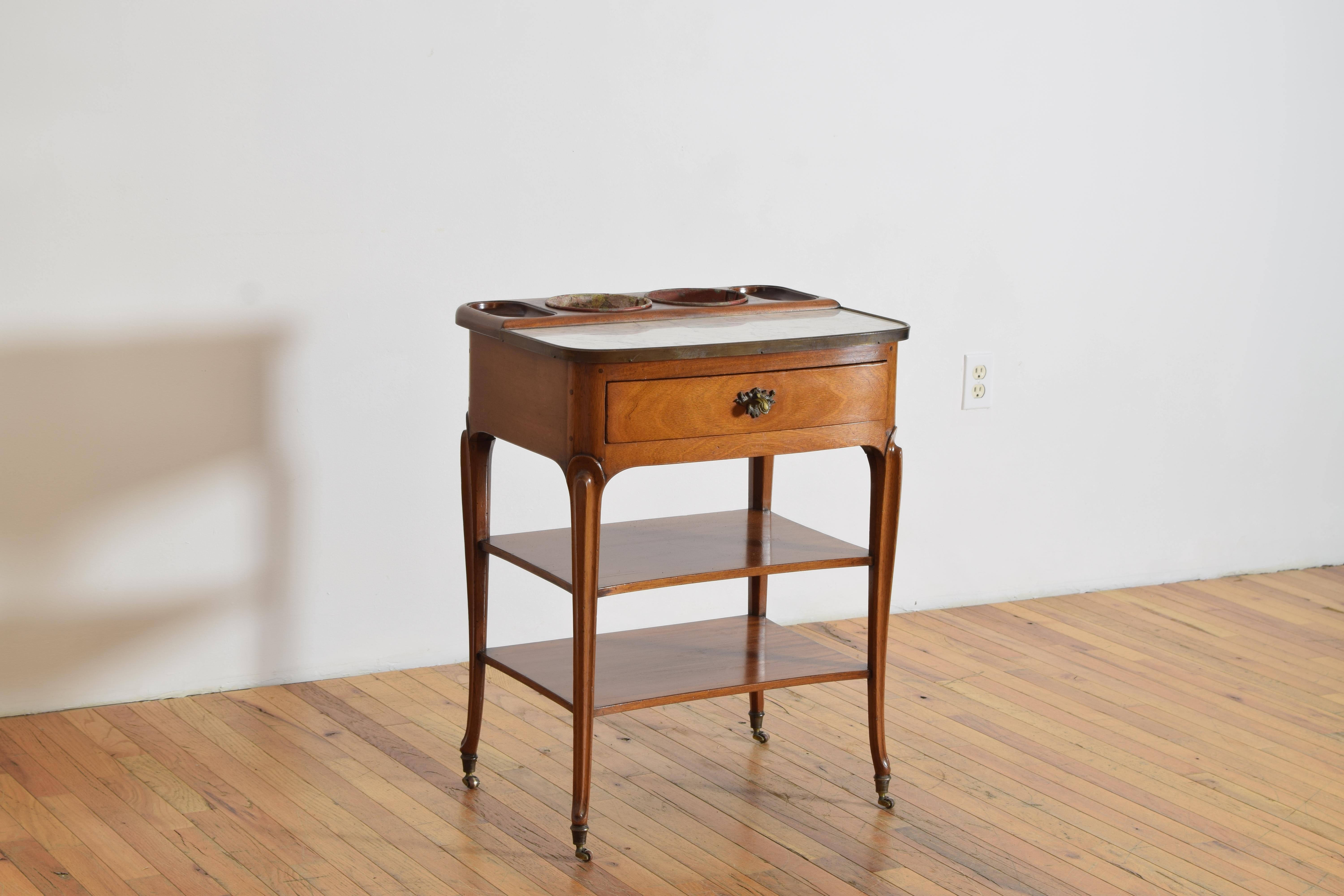 Construida en madera maciza de nogal claro, tiene una encimera rectangular de mármol con esquinas redondeadas y rematadas en latón; en la parte posterior de la encimera hay dos recipientes circulares de zinc para botellas de vino, centrados entre